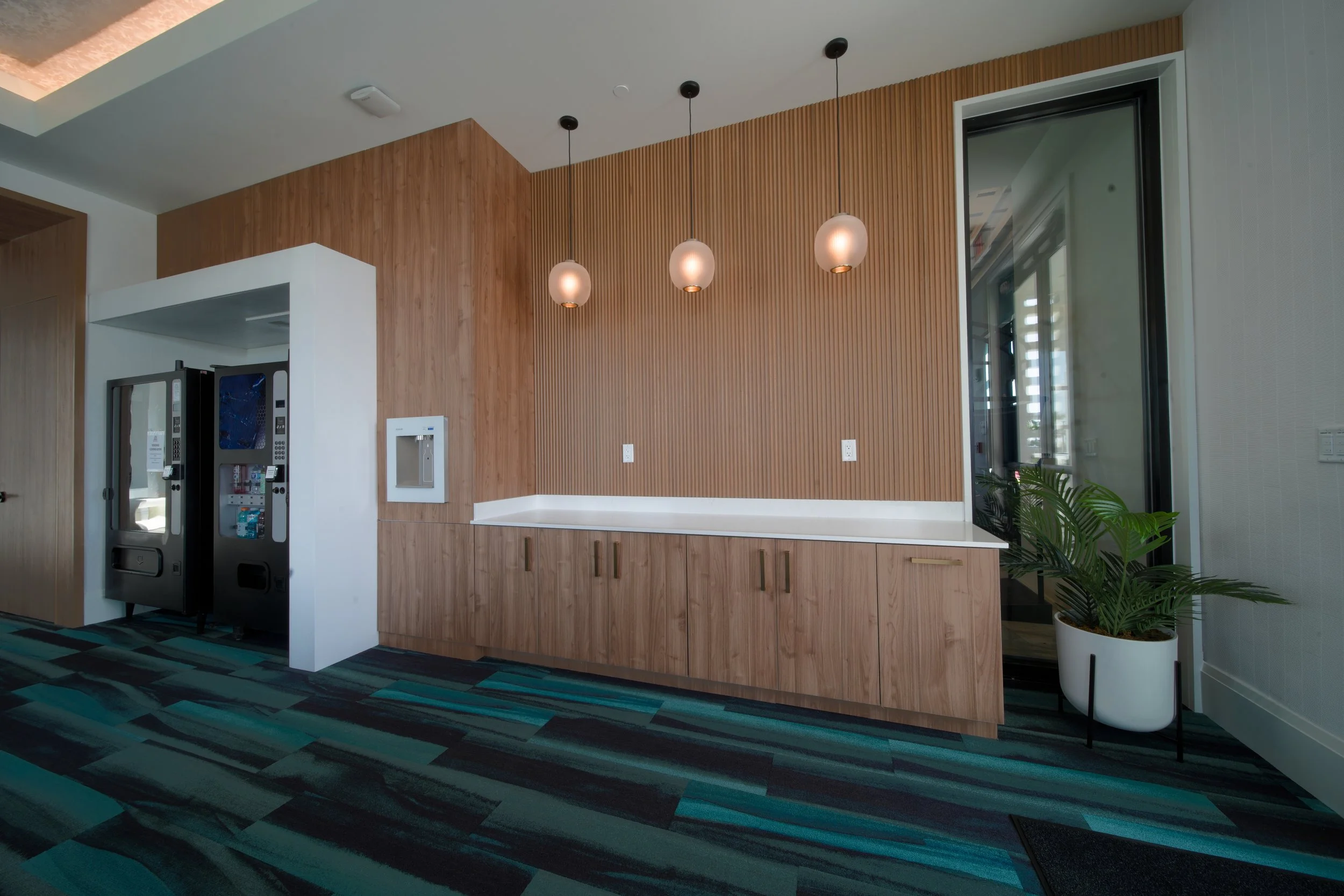 Interior of a modern space with a wooden accent wall, three hanging pendant lights, a white countertop, and a potted plant near a glass door or window.