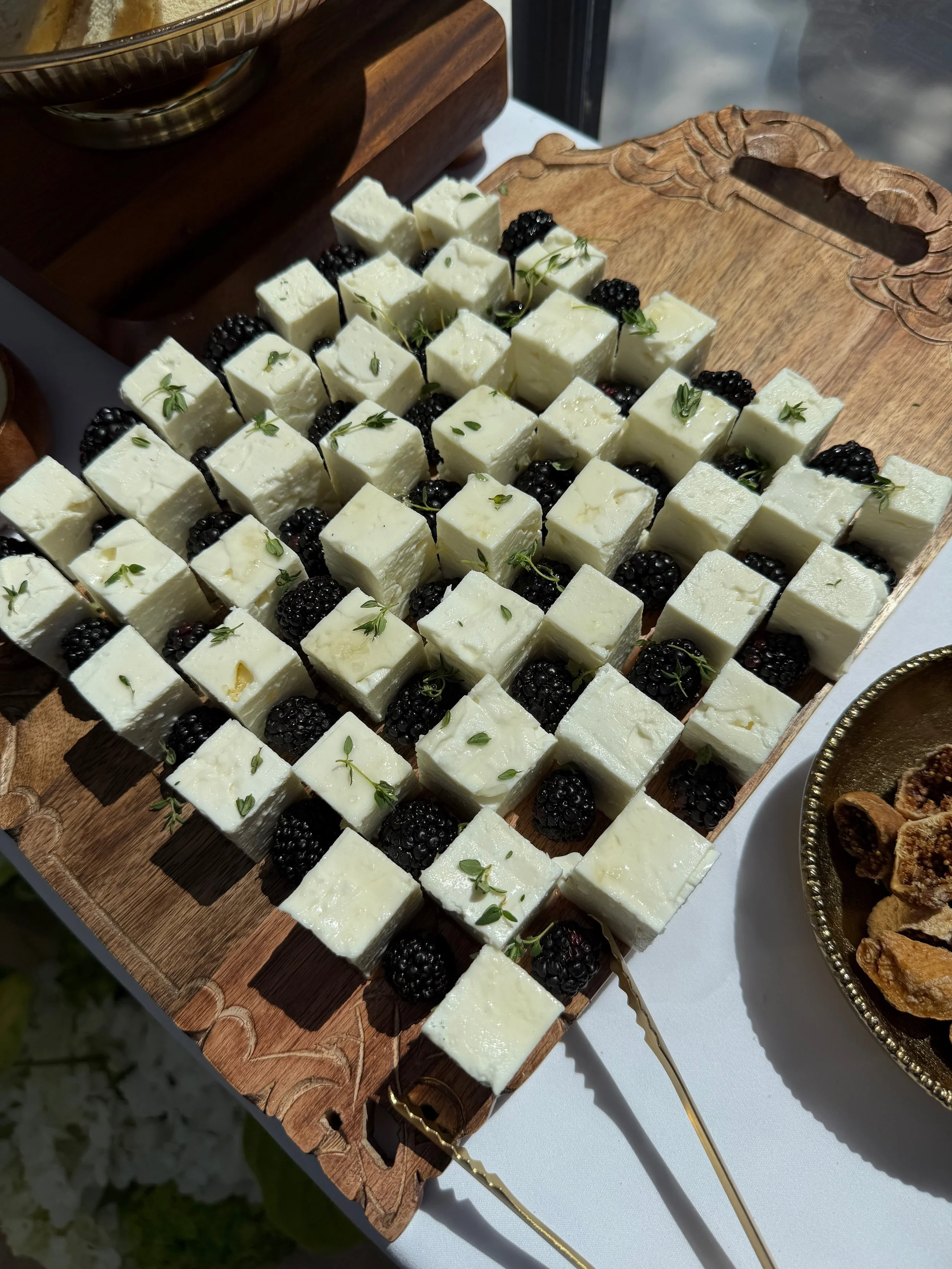 Assorted cheese cubes garnished with blackberries and small green herbs on a wooden serving board.