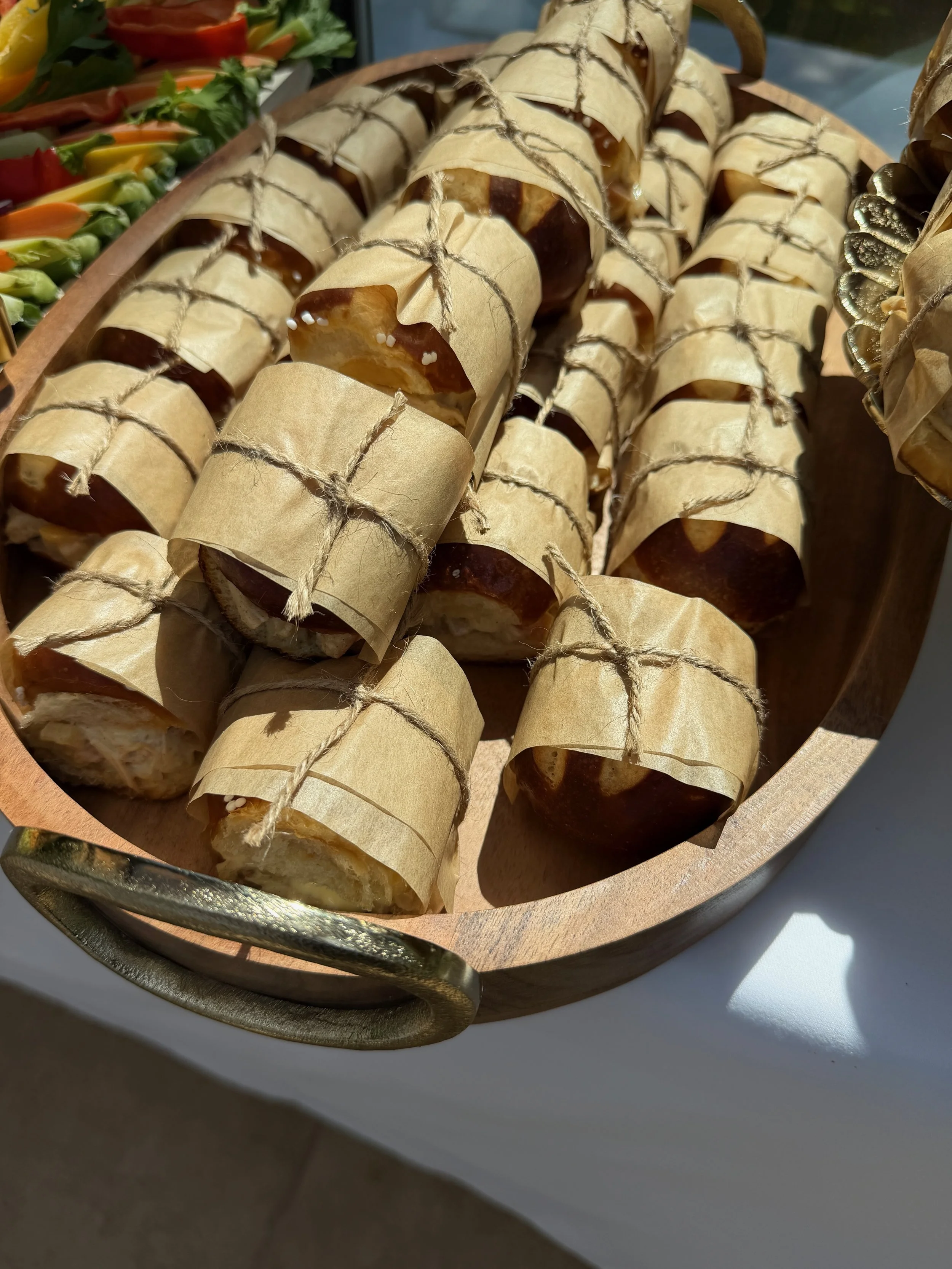 Close-up of several caramel apples wrapped in parchment paper and tied with twine, arranged in a wooden basket.