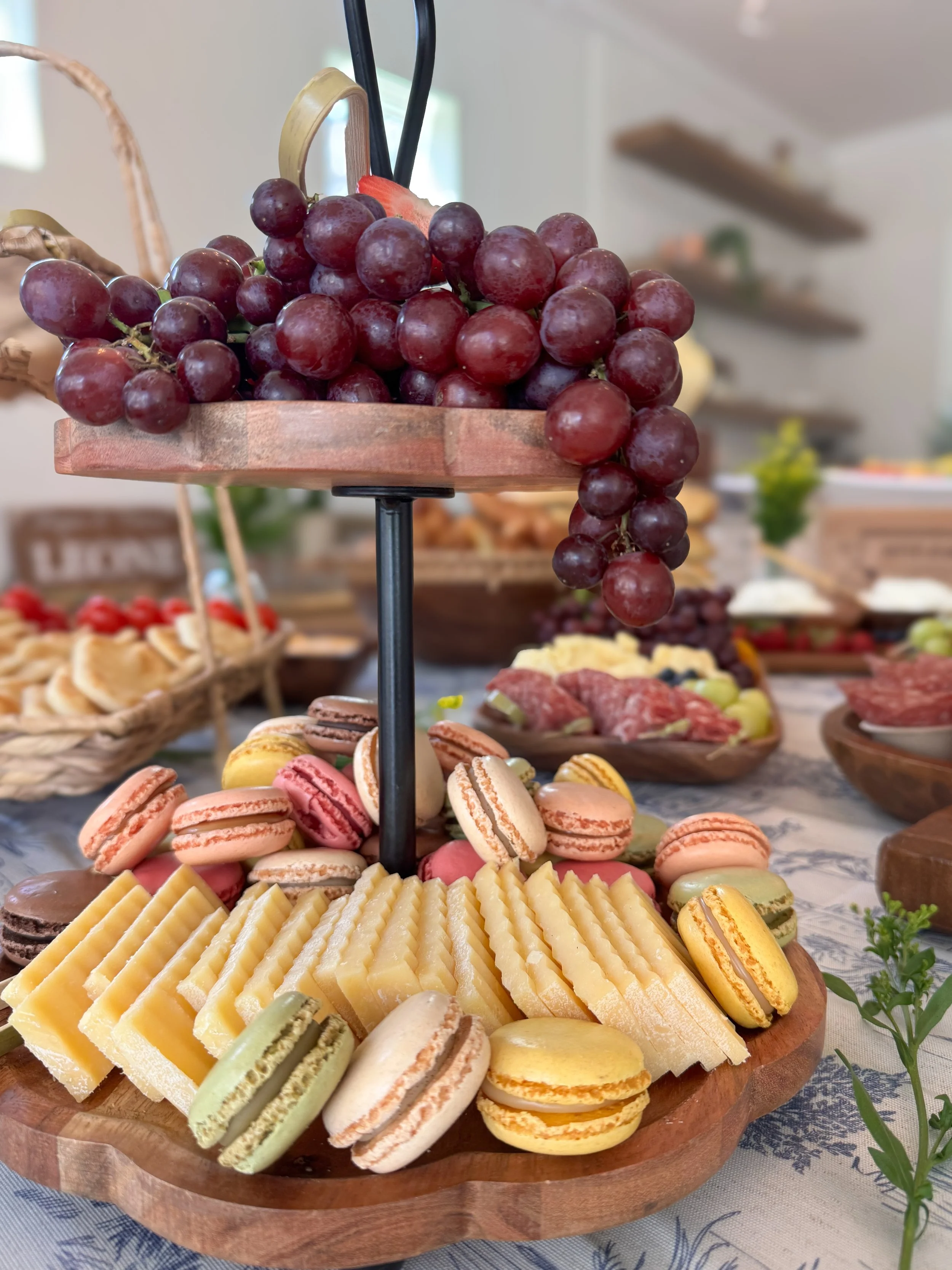 Assorted cheeses, macarons, and grapes on a wooden serving platter at a buffet table.