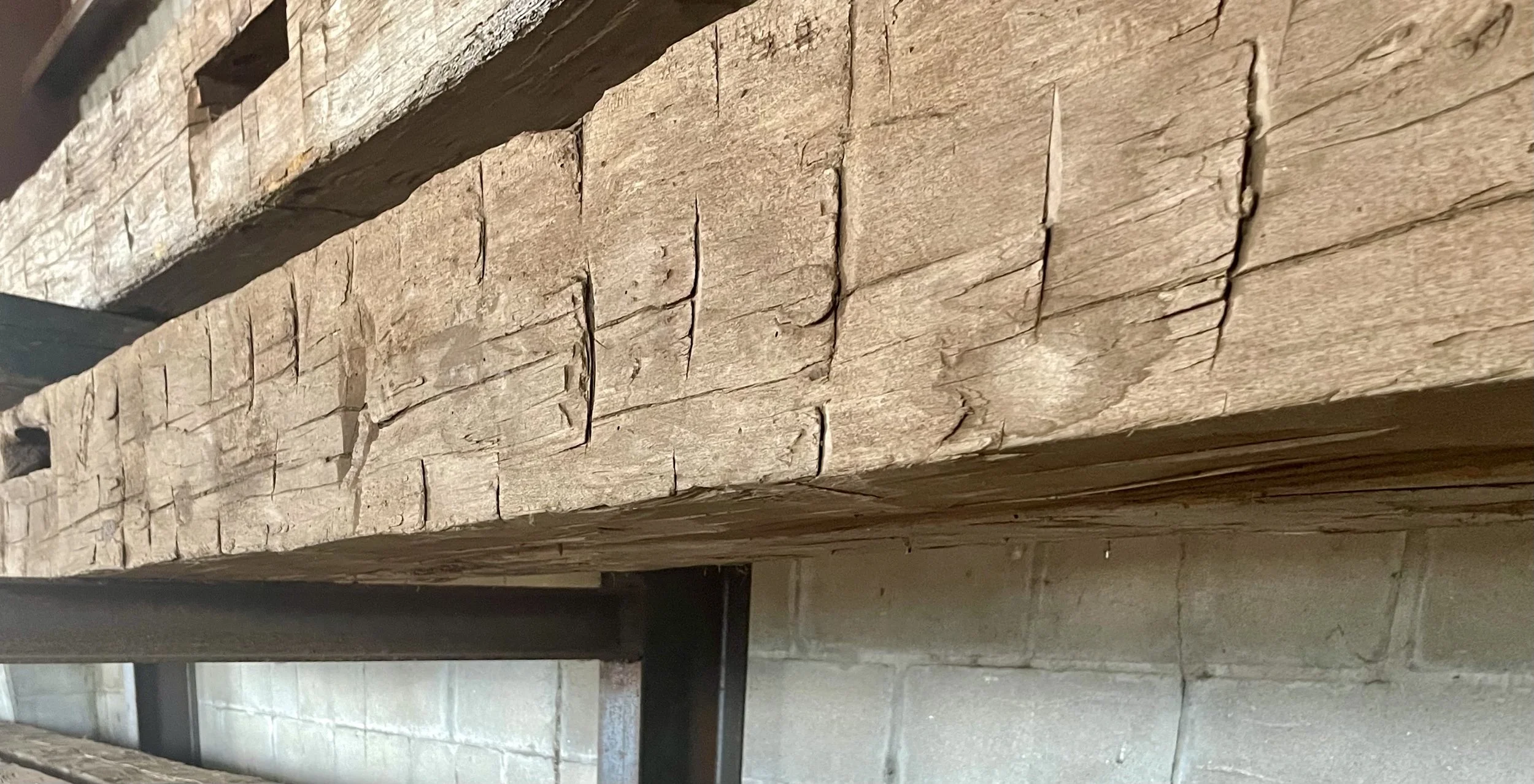 Close-up of aged, weathered wooden planks with visible cracks, stacked on metal supports, against a brick wall background.