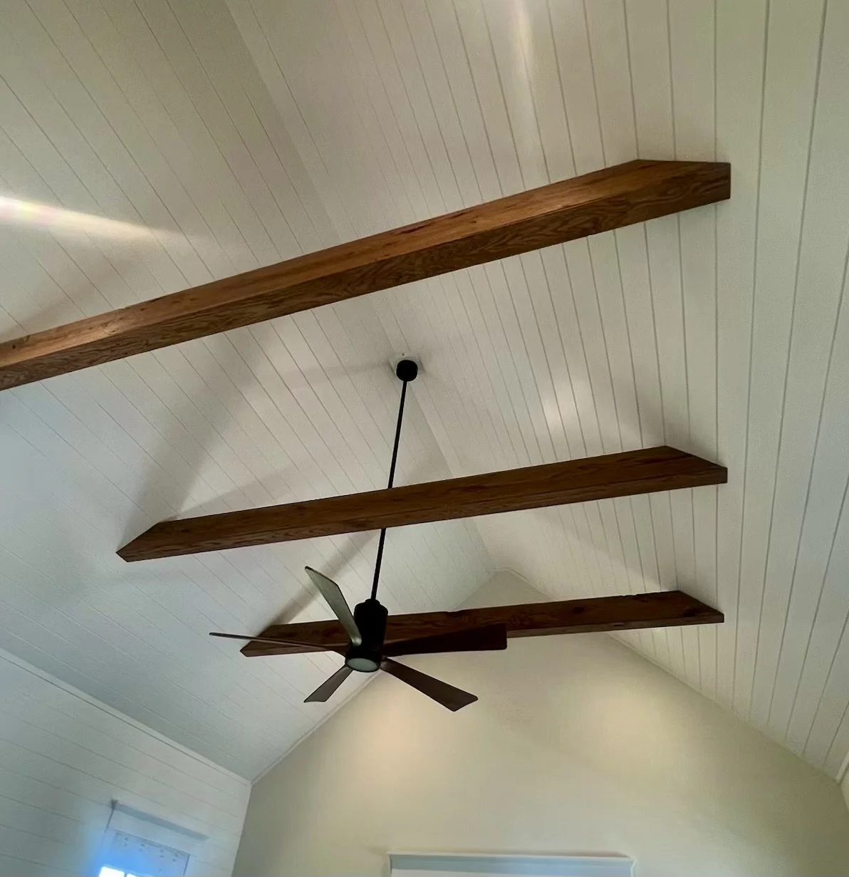 Ceiling with white wood paneling, three large wooden beams, a black ceiling fan with five blades, and a black pendant light hanging in the center.