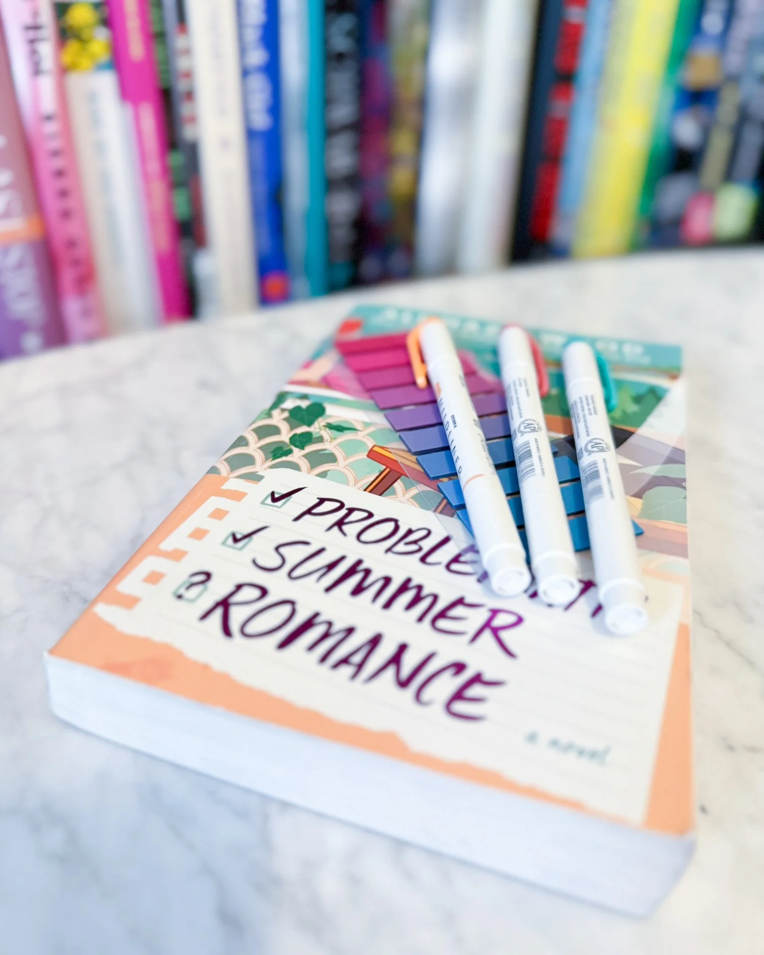 The book problematic summer romance by Ali Hazelwood on a marble coffee table with colorful tabs and highlighters for annotation on top