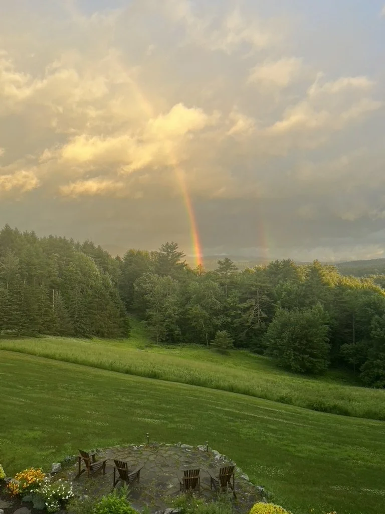 Image of a rainbow over trees and a green field.