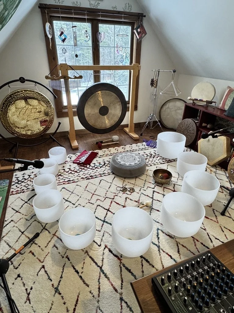 Image of a room with a window that contains a rug, ten crystal singing bowls, gongs and various other instruments