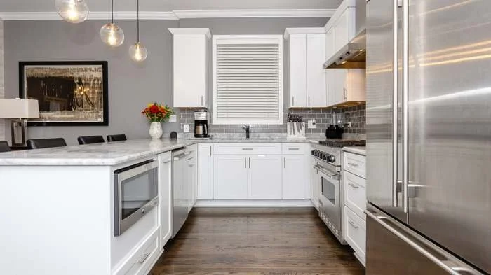 Modern kitchen with white cabinets, stainless steel appliances, gray subway tile backsplash, hardwood flooring, and a gray wall.