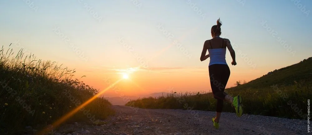 A woman runs on a gravel road at sunset.