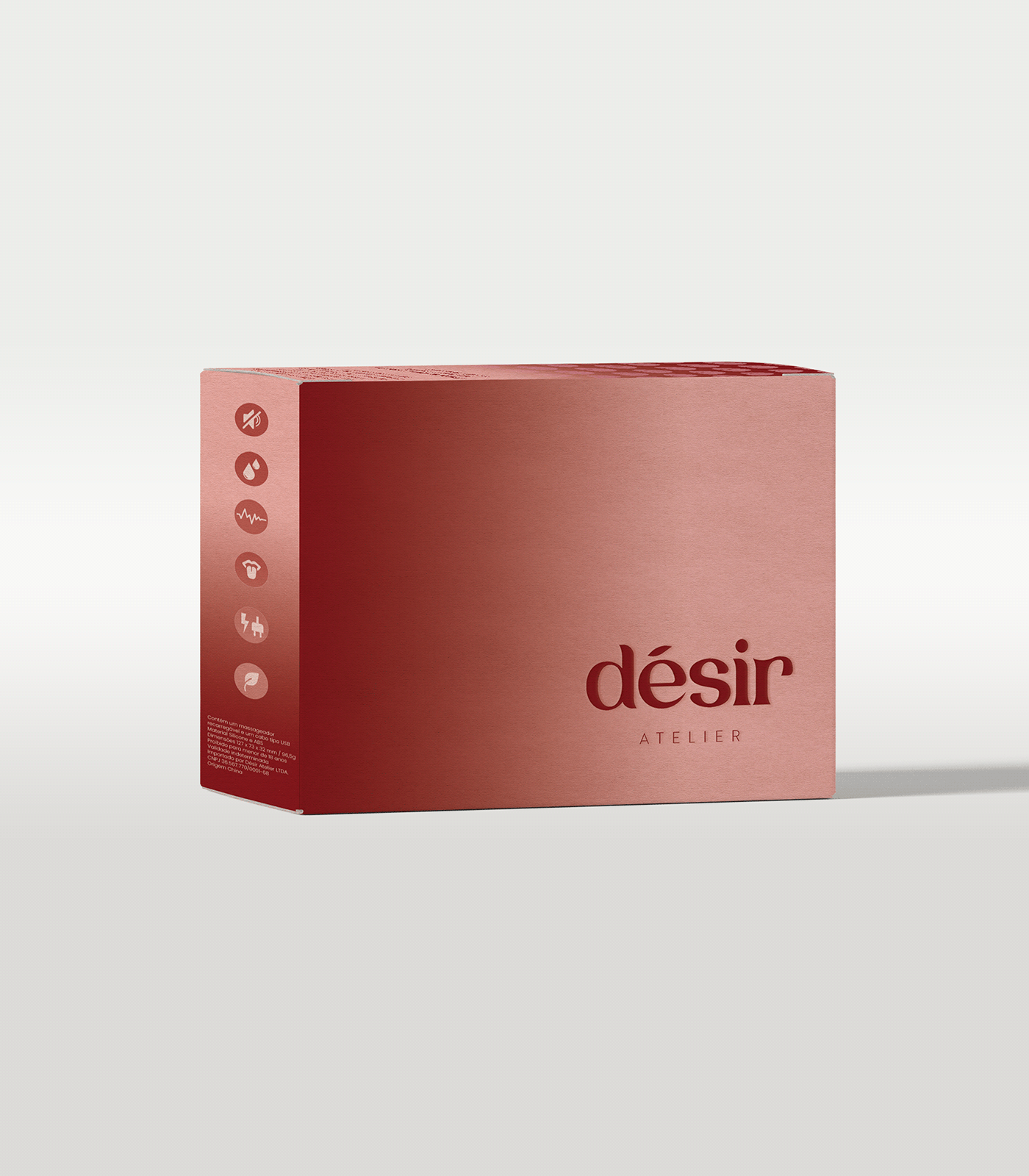 Embalagem de produto chamado 'désir' da marca ATELIER, na cor rosa, com ícones na lateral que indicam características do produto, como não causar irritação, ser para uso externo, monitorar a frequência cardíaca, e seu peso. A embalagem está posicionada em um fundo cinza claro.
