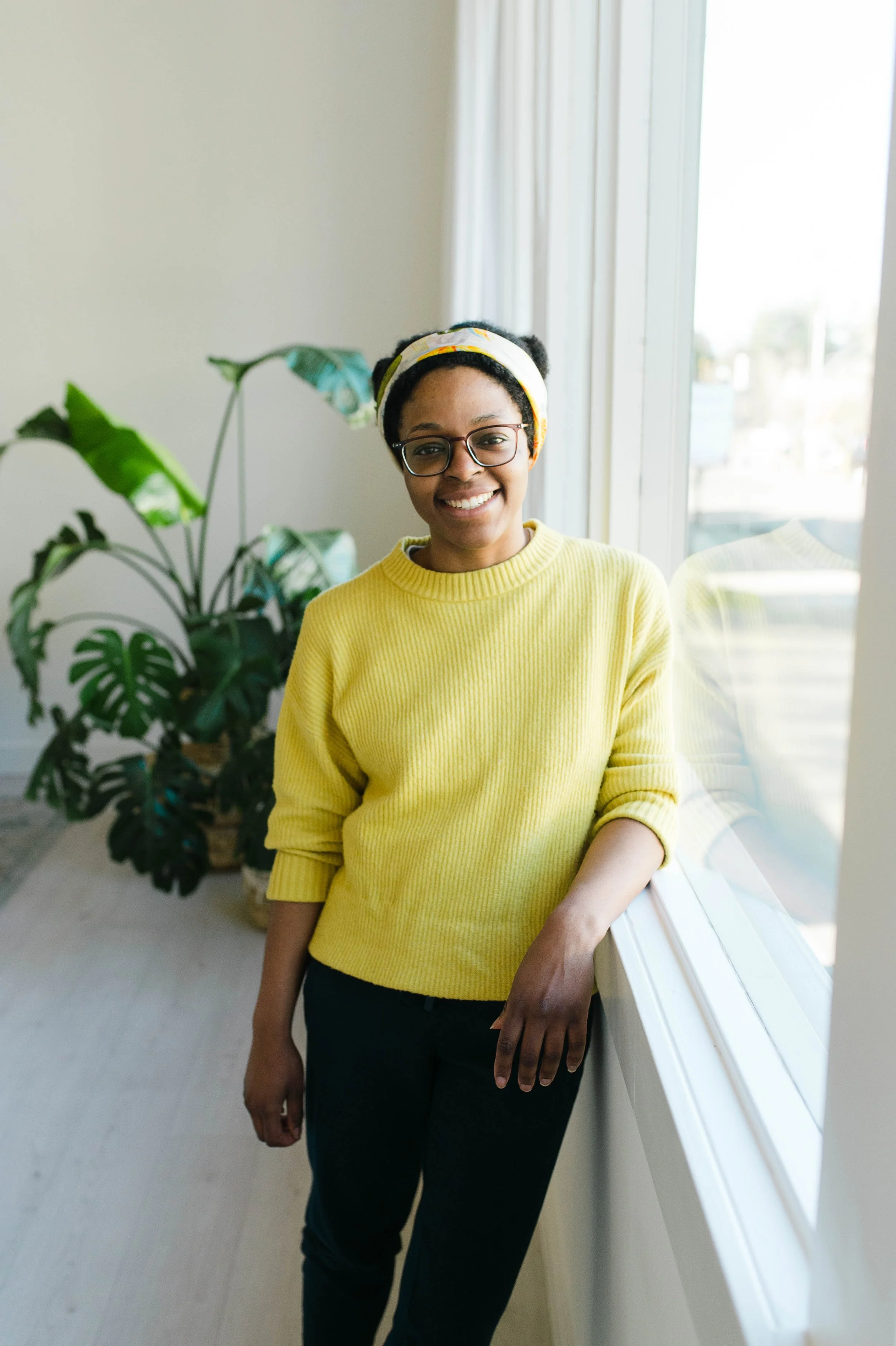 Aneisha, black woman with natural hair wearing a yellow sweater, smiles.