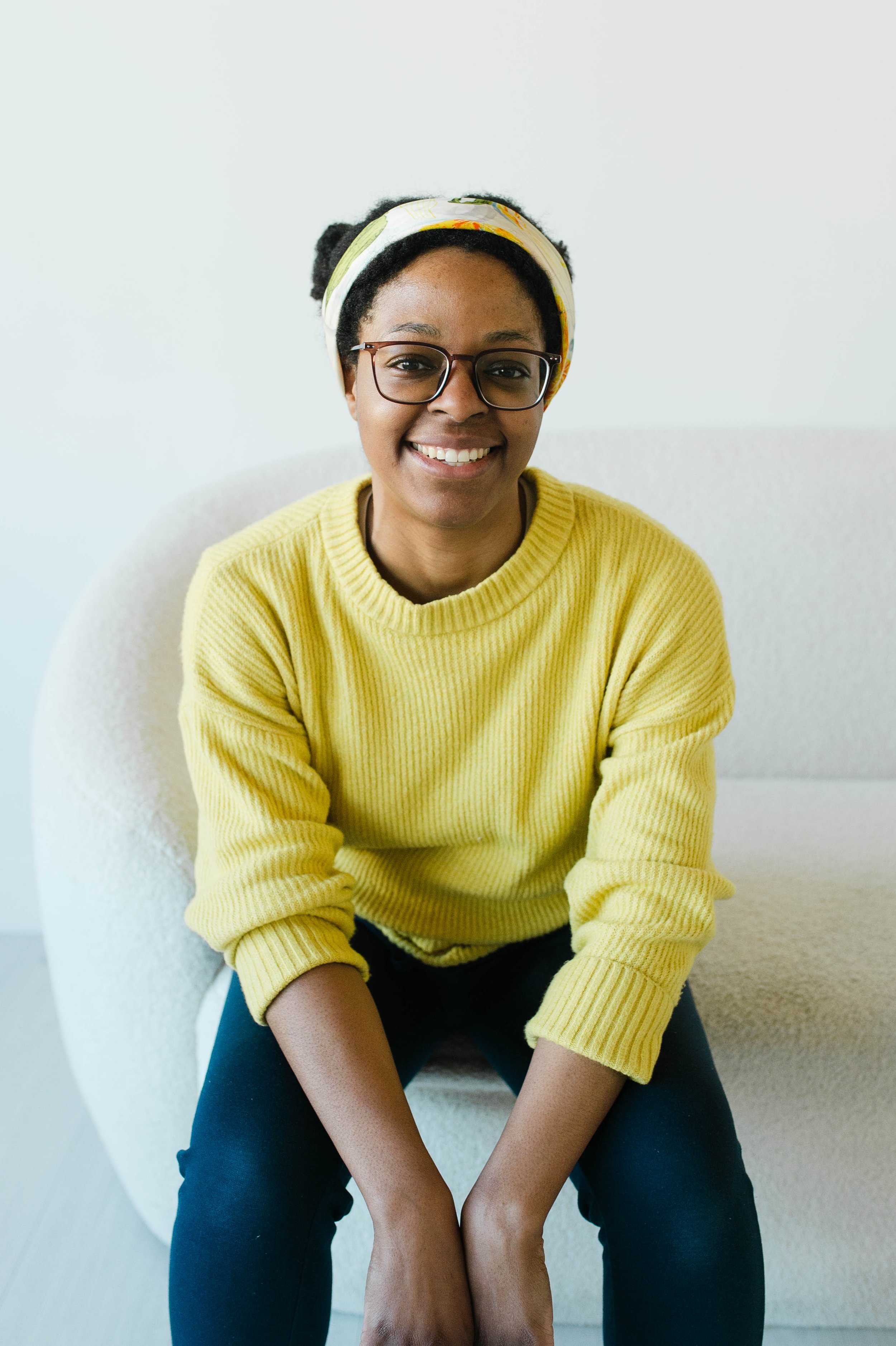 Aneisha, black woman with natural hair wearing a yellow sweater, smiles.