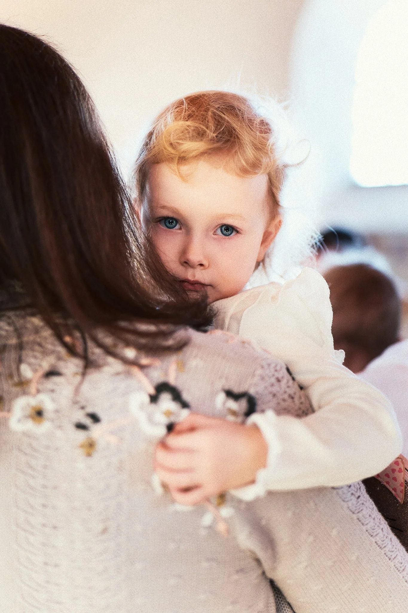 Kleines Mädchen mit blonden Haaren und blauen Augen, das eine Frau umarmt.