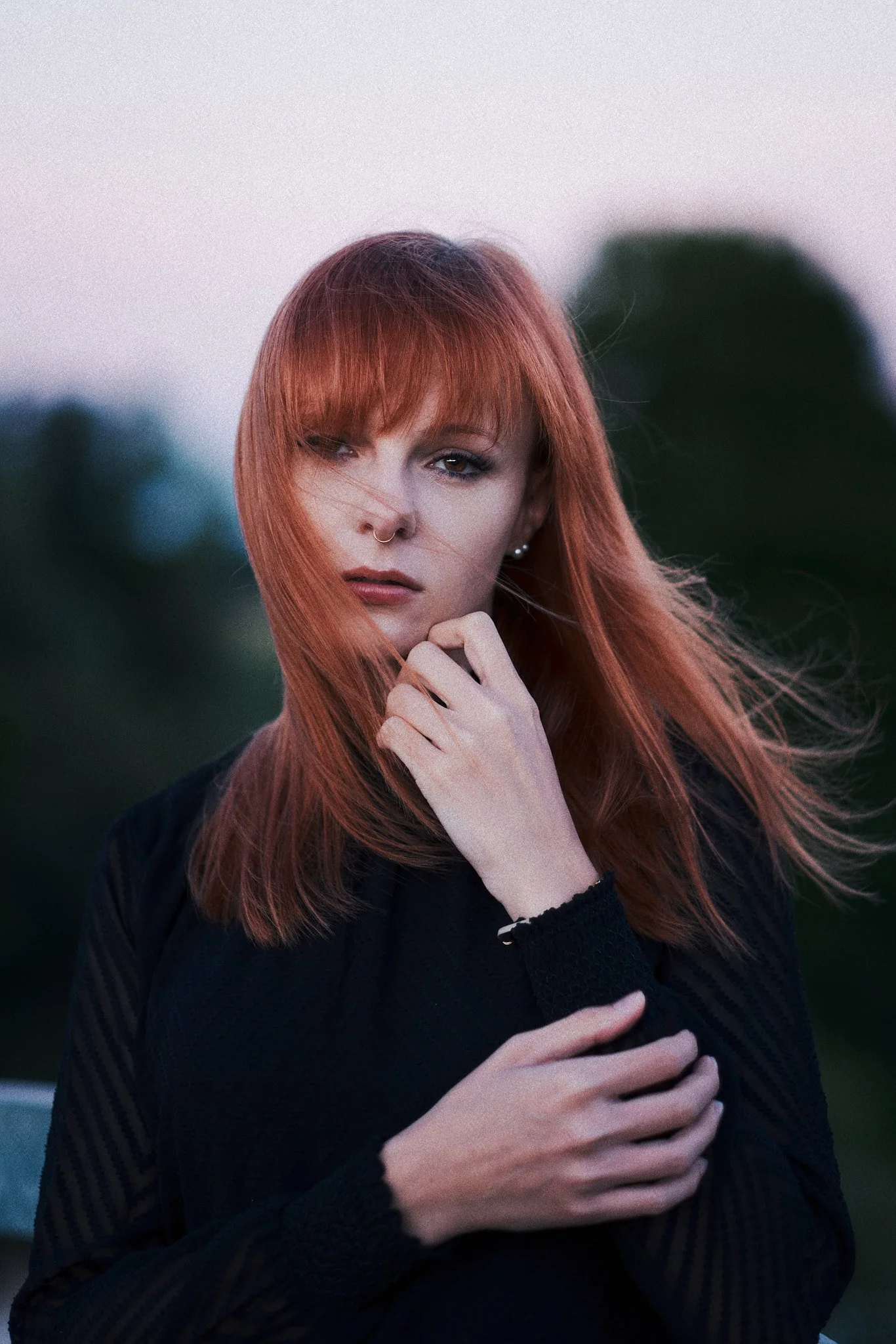 Frau mit roten Haaren, schwarzer Pullover, outdoors bei Sonnenuntergang, Hand auf ihrer Brust, nachdenklich.