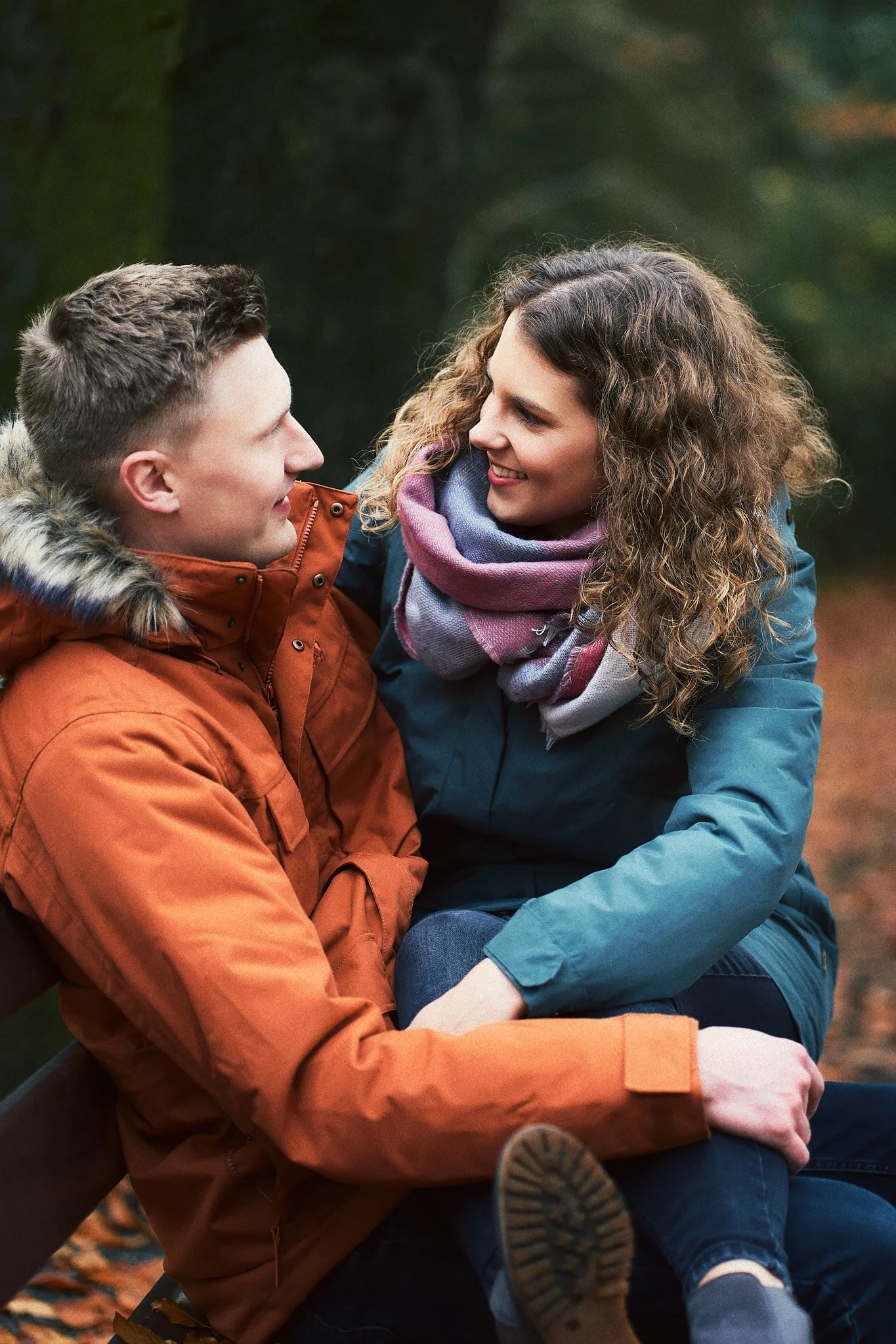 Ein Mann und eine Frau sitzen sich auf einer Bank im Park gegenüber, lächeln sich an und schauen sich an.