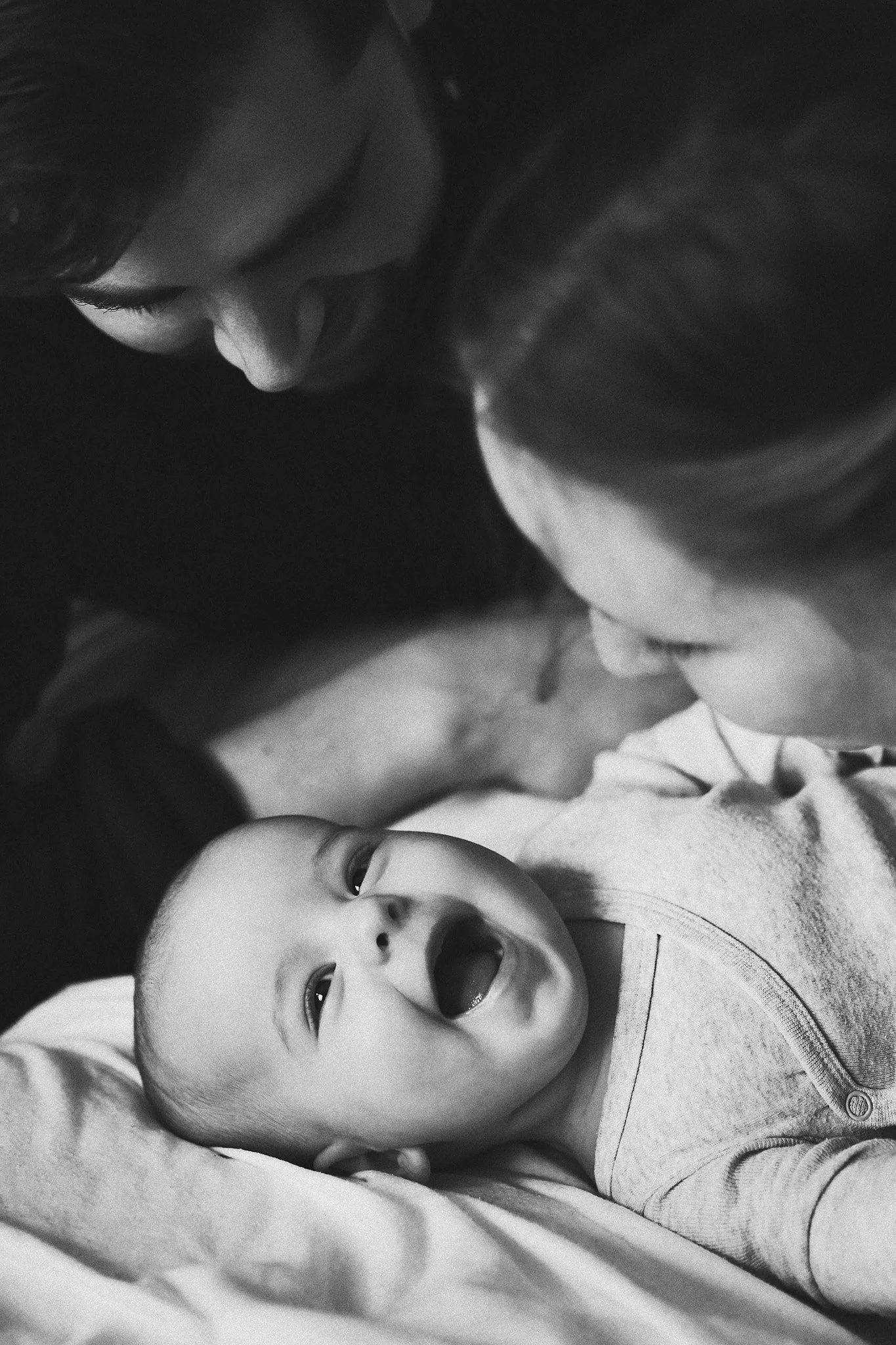 Ein Baby liegt auf einer Person, die zu ihm herunterblickt, und schaut neugierig.