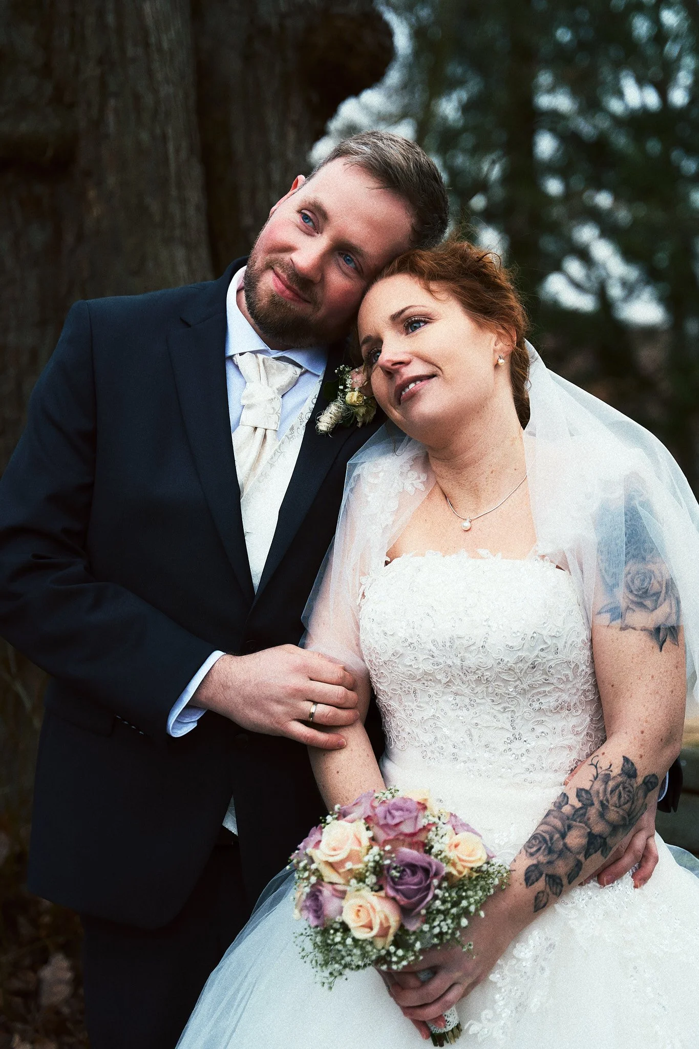 Ein Brautpaar bei einer Hochzeit, der Mann trägt einen schwarzen Anzug und die Frau trägt ein weißes Hochzeitskleid, sie hält einen Blumenstrauß.