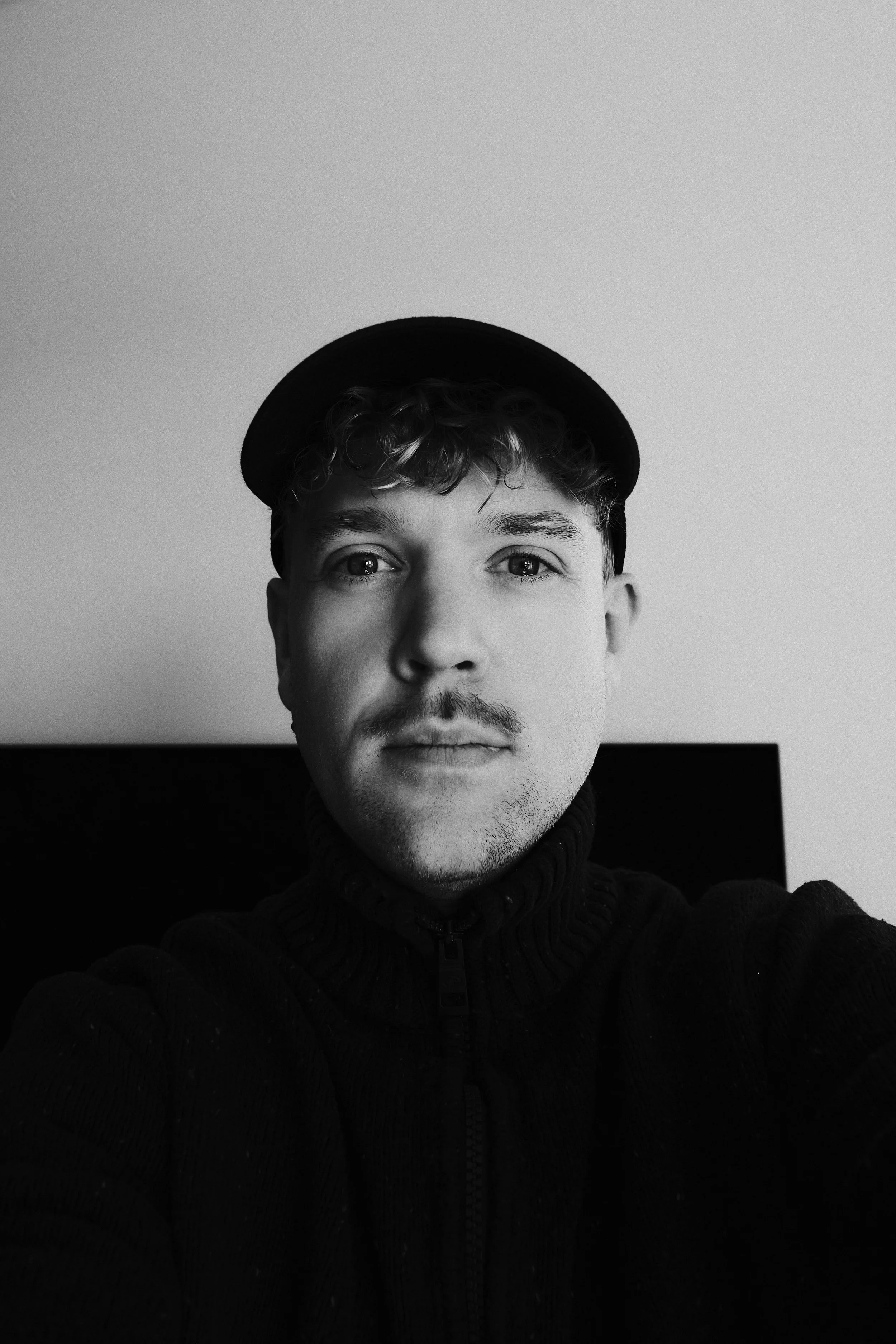 Schwarz-weiß-Foto eines jungen Mannes mit einem dunklen Hut und einer dunklen Zipfelmütze, der direkt in die Kamera lächelt.