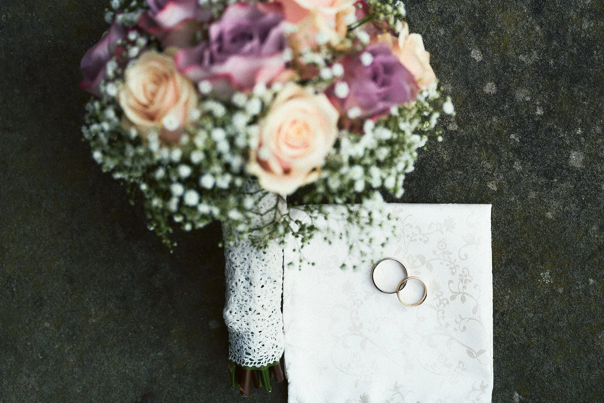 Hochzeitsring auf einer weißen Serviette neben einem Blumenstrauß aus Rosen und kleinen weißen Blumen.