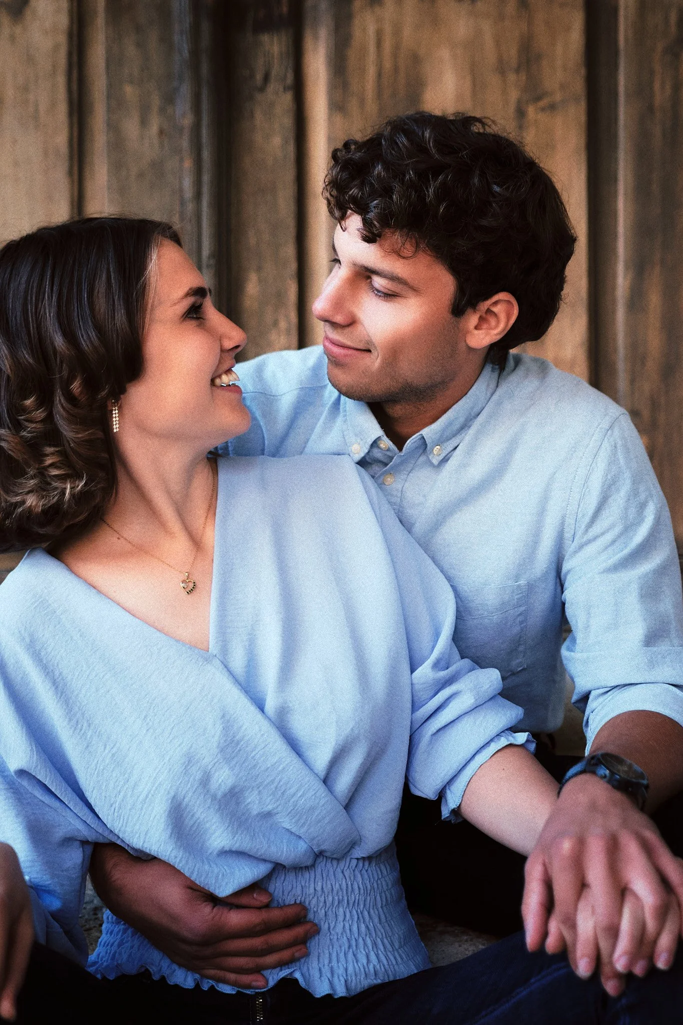 Ein Paar, das sich liebevoll ansieht und hält, sitzen gemeinsam vor einer Holzwand.