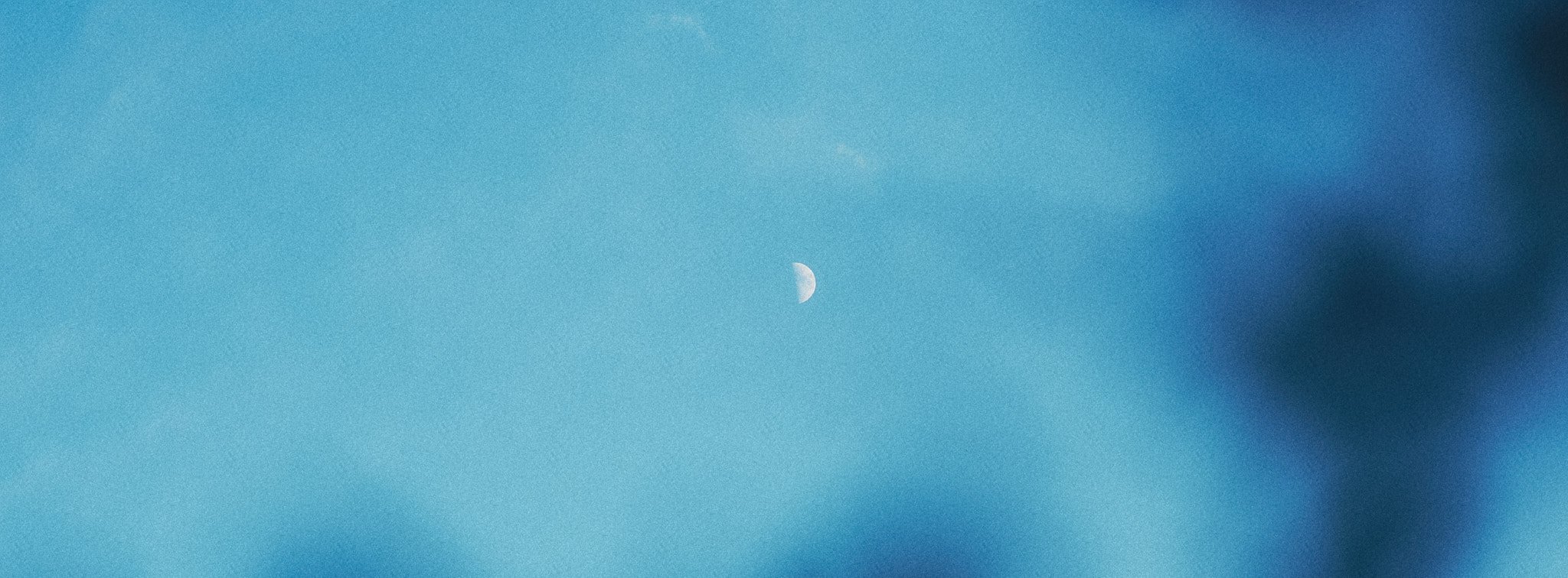 Halbmond im blauen Himmel, teilweise von Wolken verdeckt