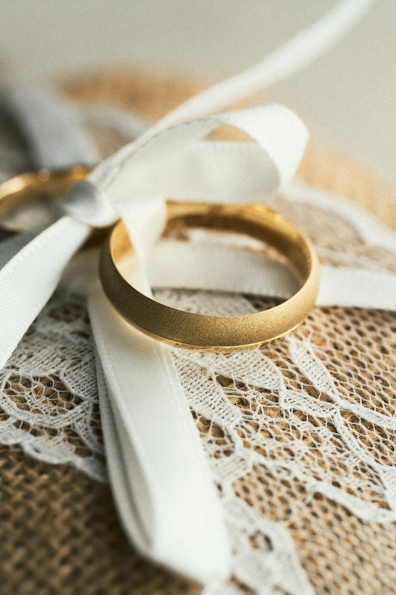 Goldene Ehering auf Spitzenware mit weißen Bändern und Schleifen.