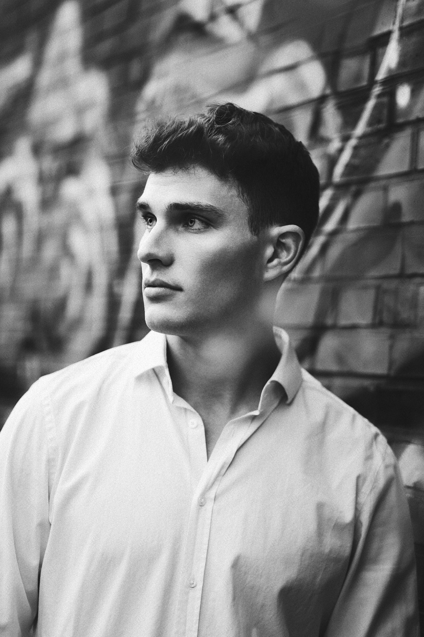 Schwarz-Weiß-Fotografie eines jungen Mannes, der nach links schaut, vor einer Hauswand mit Spiegelbildern, Ziegelsteinen und einem Davidstern.