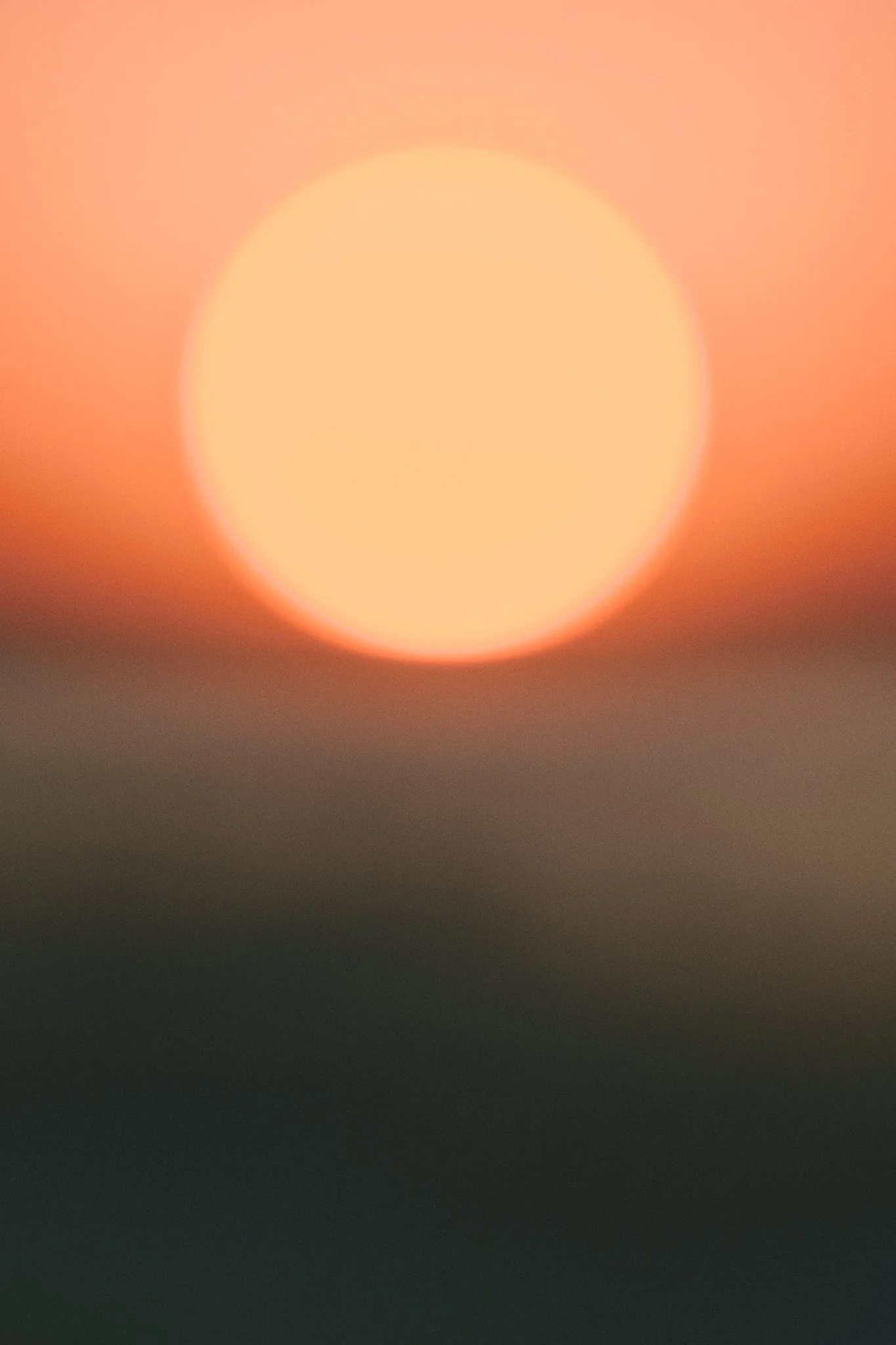 Unscharfer Sonnenuntergang mit orangem Himmel und großer, runder Sonne