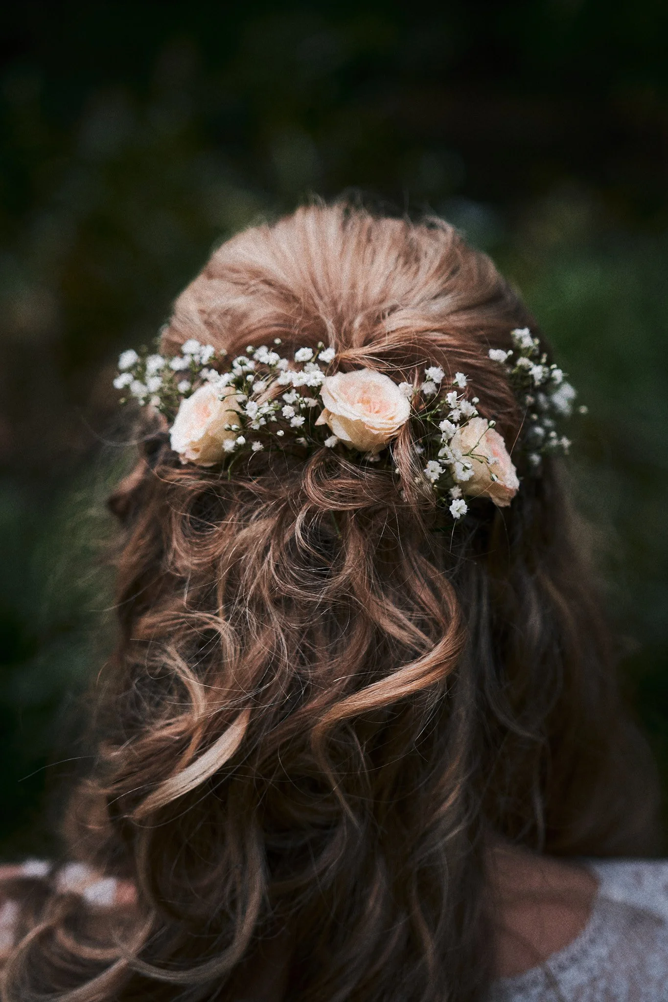 Haare einer Person mit einer Haarkrone aus weißen Blumen und kleinen weißen Blüten, gegen einen dunklen Hintergrund.