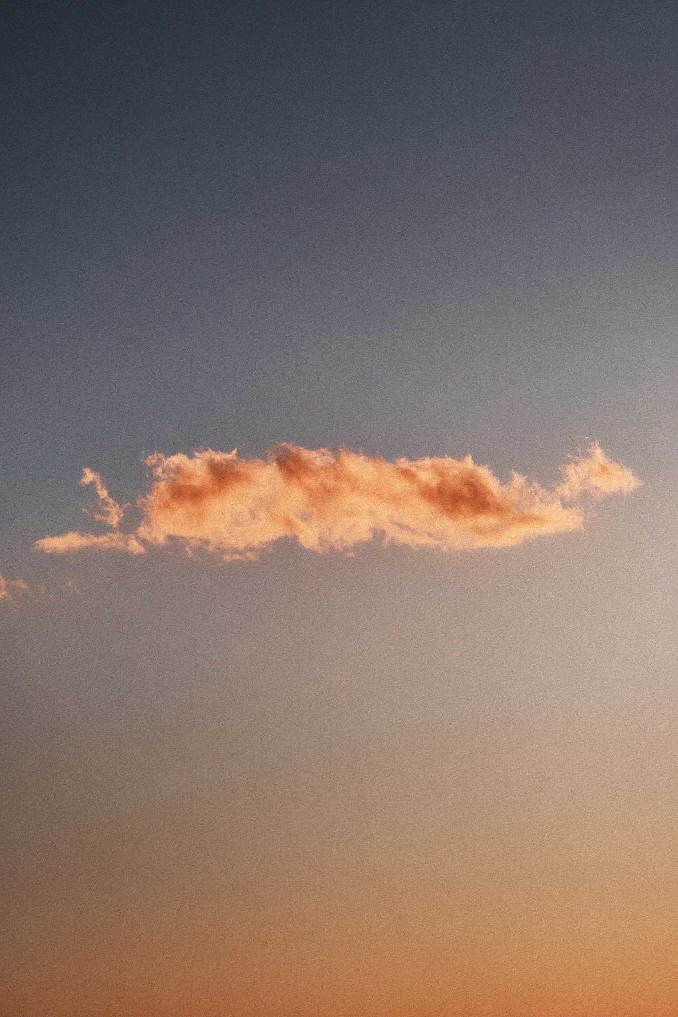 Ein einzelnes orangefarbenes Wolkenstück am Himmel während der Dämmerung
