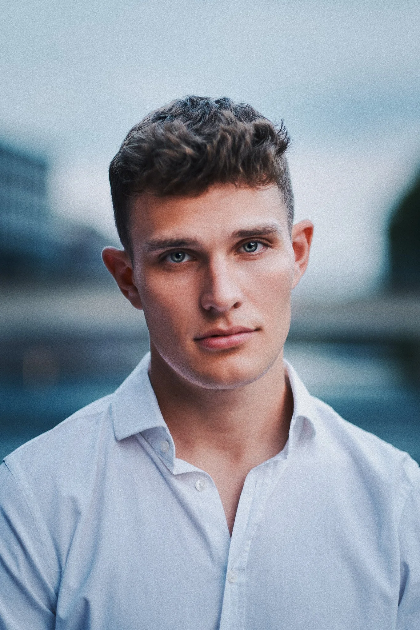 Porträt eines jungen Mannes mit kurzen, braunen Haaren, blauen Augen und heller Haut, trägt ein weißes Hemd.