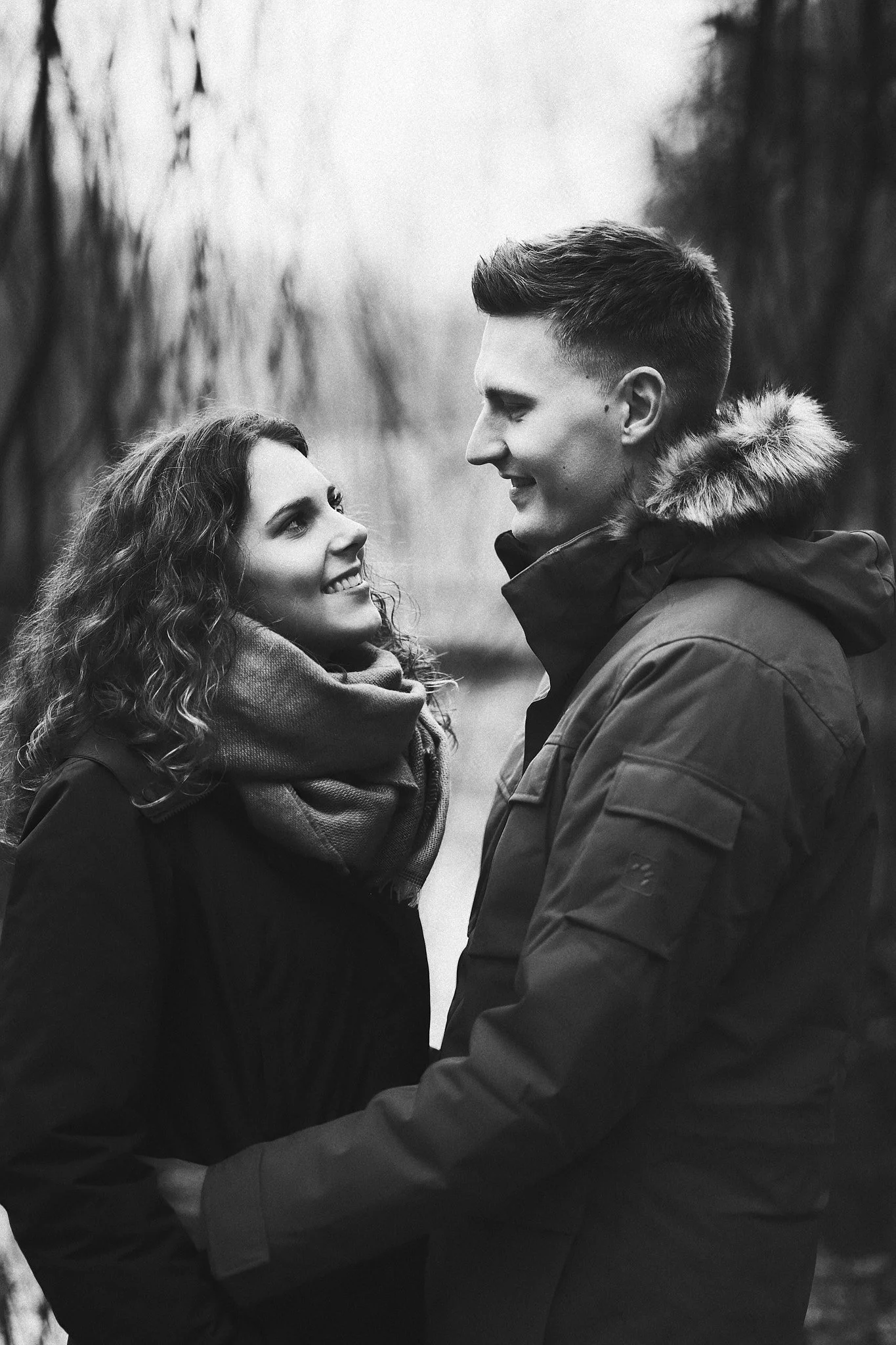 Ein glückliches Paar, das sich im Freien umarmt und anlächelt, im Winter mit warmen Jacken.