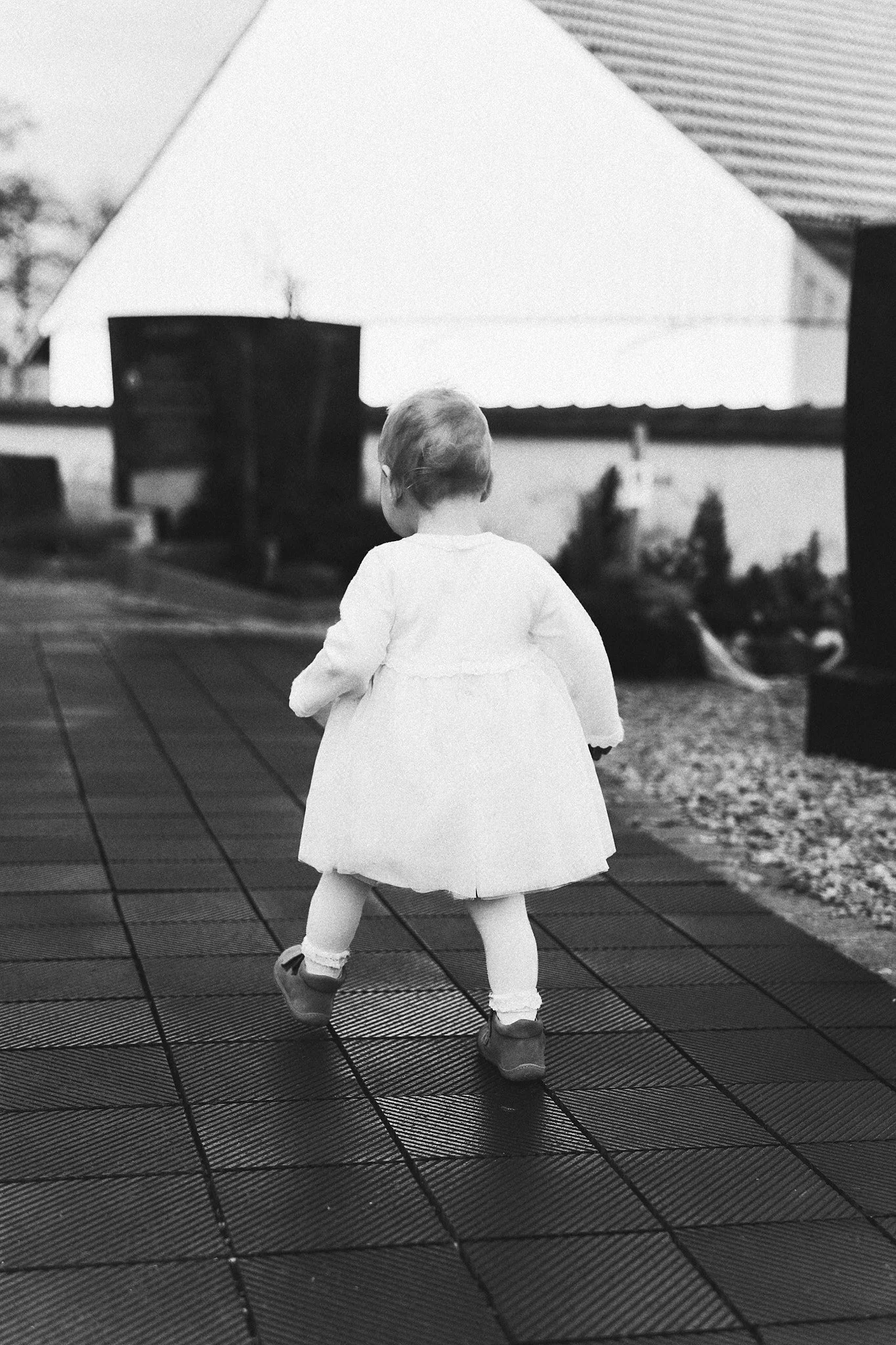 Ein junges Mädchen in einem weißen Kleid läuft auf einer beweglichen Oberflächenfläche im Freien, im Hintergrund sind Bäume und ein Gebäude sichtbar.