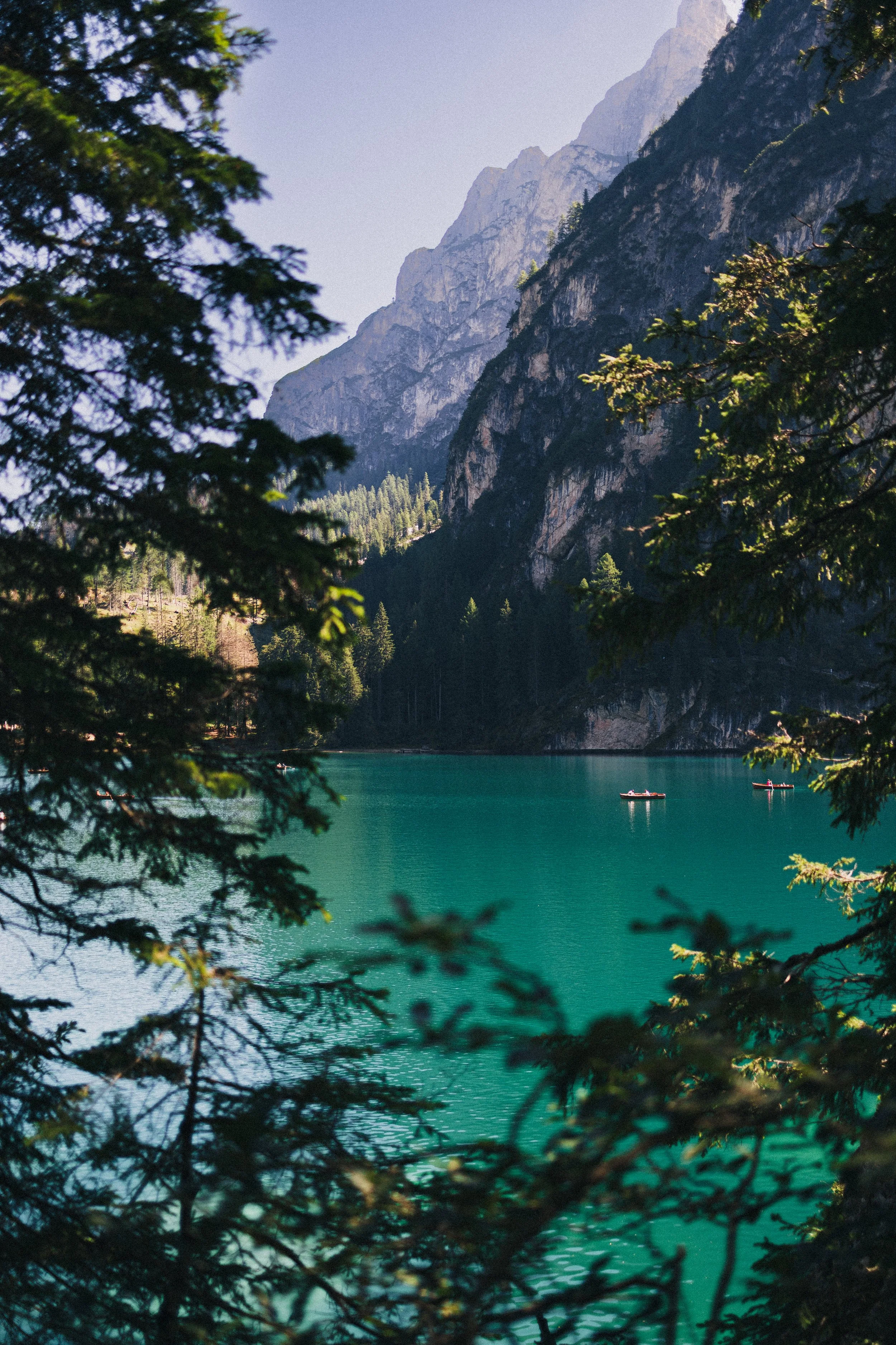 Blick auf einen ruhigen, grünen See im Gebirge, umrahmt von Tannenbäumen, mit zwei Booten auf dem Wasser und hohen Felswänden im Hintergrund.