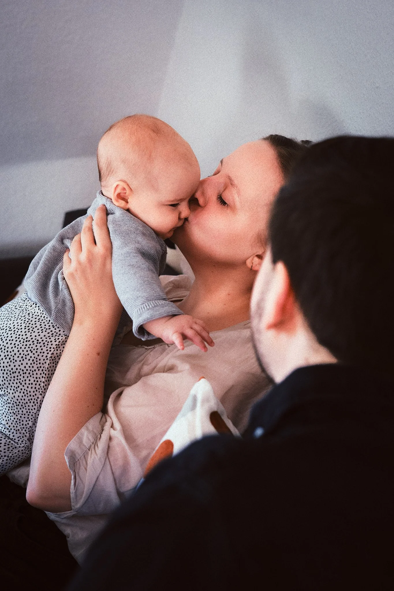 Eine Frau küsst ein Baby auf die Nase während ein Mann zuschaut.