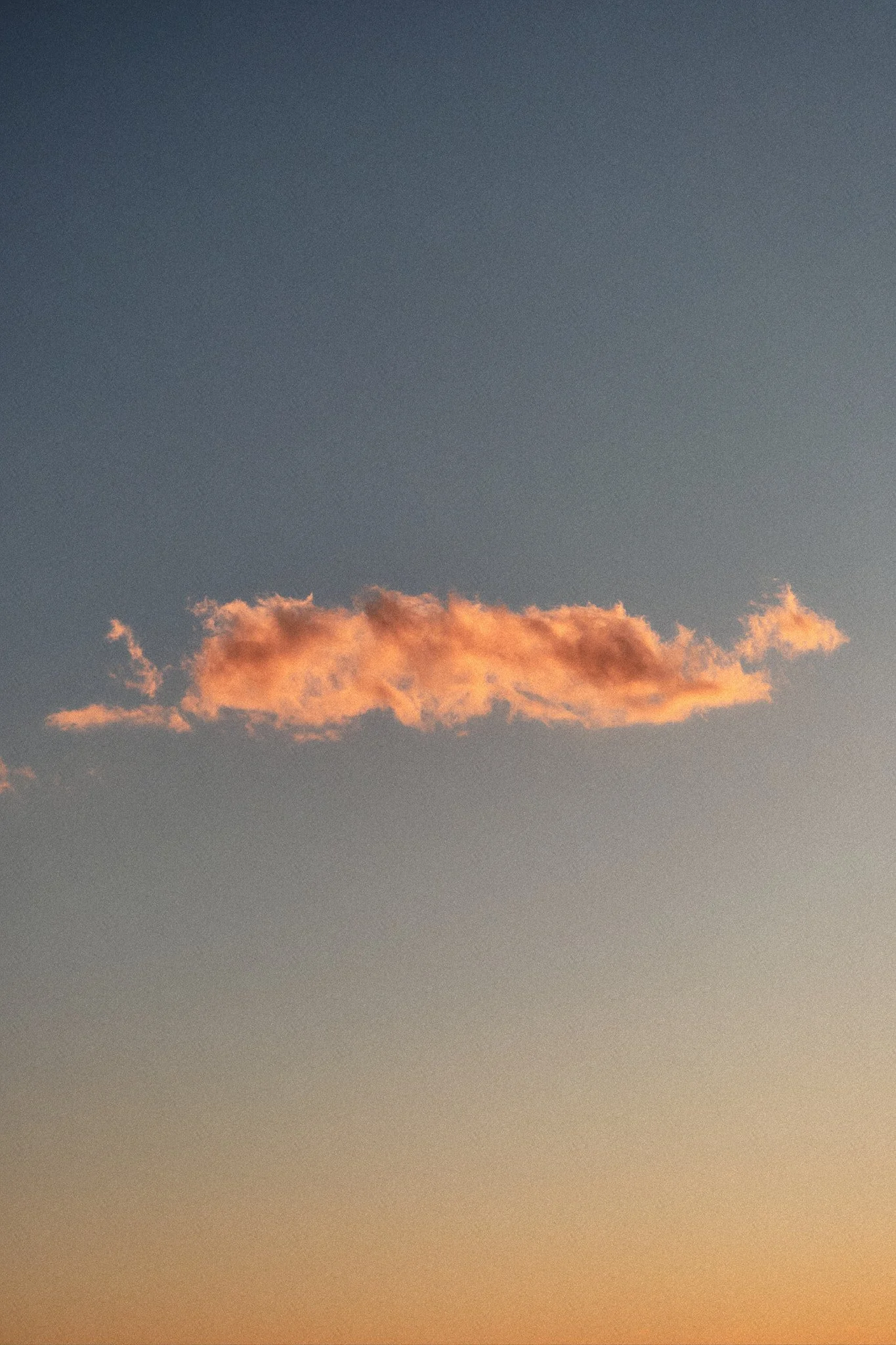 Ein einzelnes, orangefarbenes Wolkenstück am Himmel während des Sonnenuntergangs.