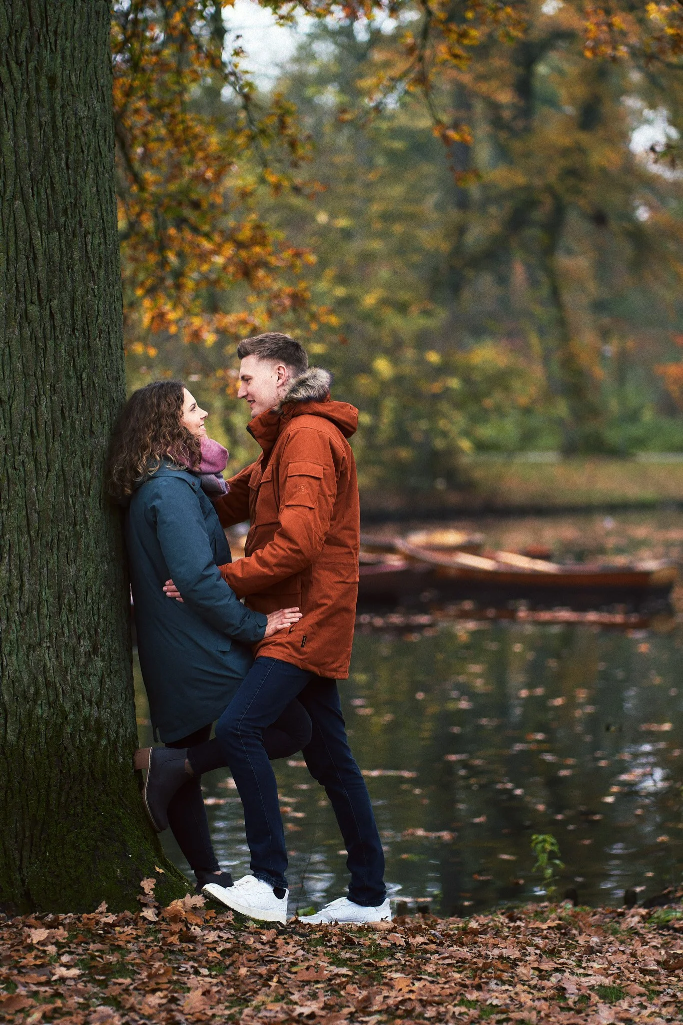 Ein Paar steht an einem Baum im Herbstwald am Fluss und schaut sich verliebt an.