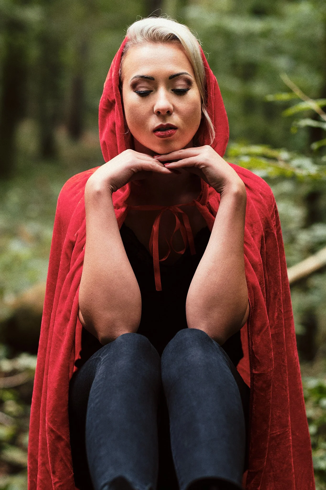 Frau in rotem Umhang sitzt im Wald, mit geschlossenen Augen.