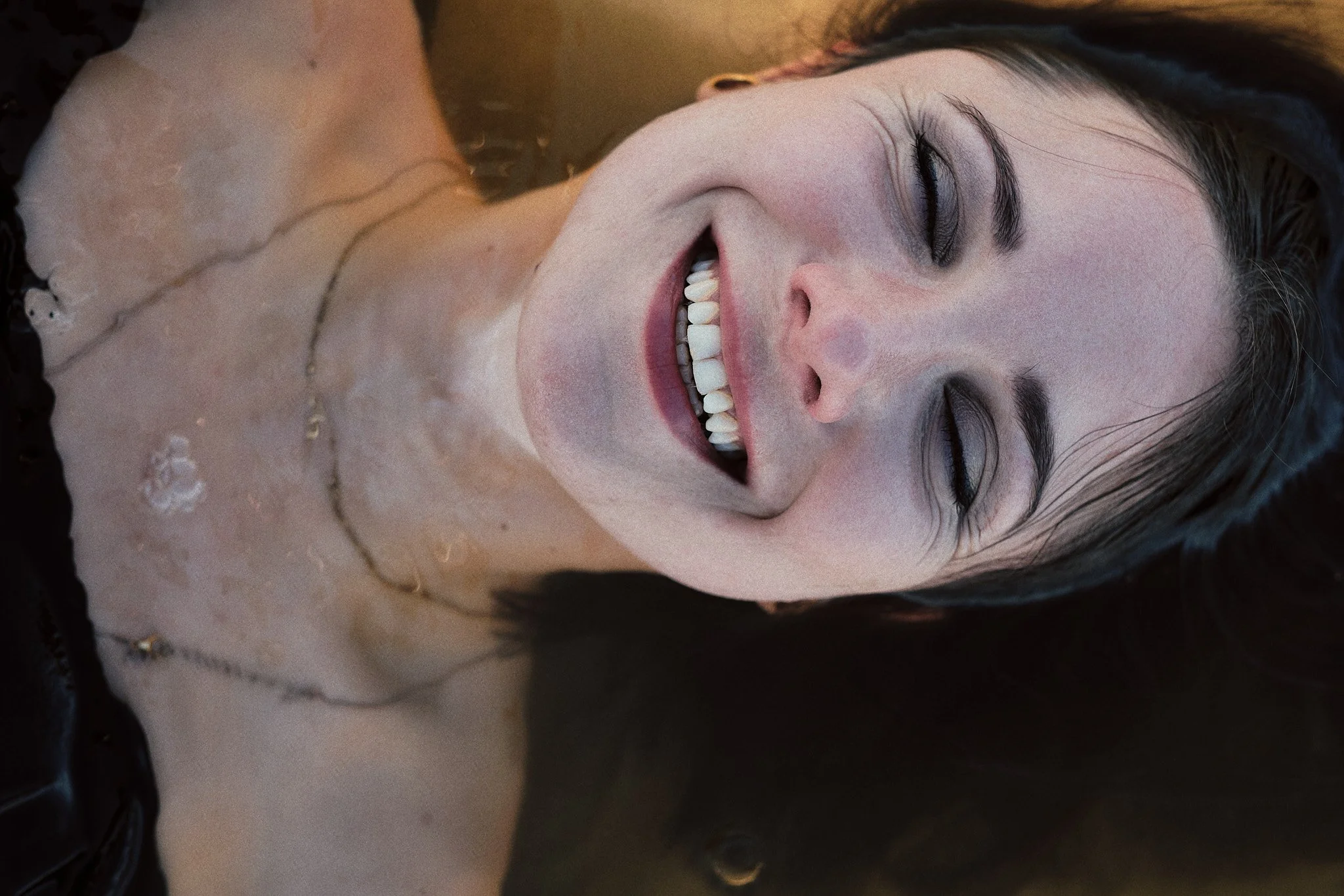 Lächelnde junge Frau mit dunklem Haar, die mit geschlossenen Augen im Wasser liegt.