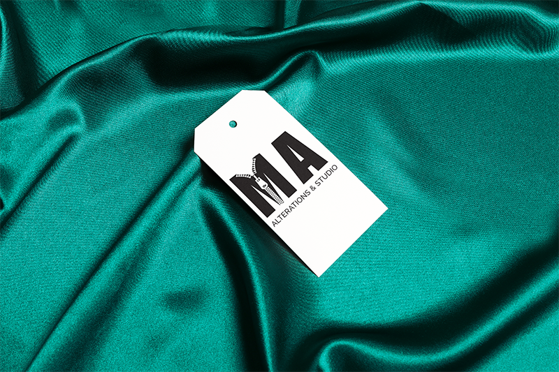 White clothing tag with black and gray logo and text on teal fabric