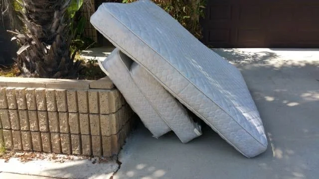 Two mattresses stacked against a concrete curb on the sidewalk outside a house.
