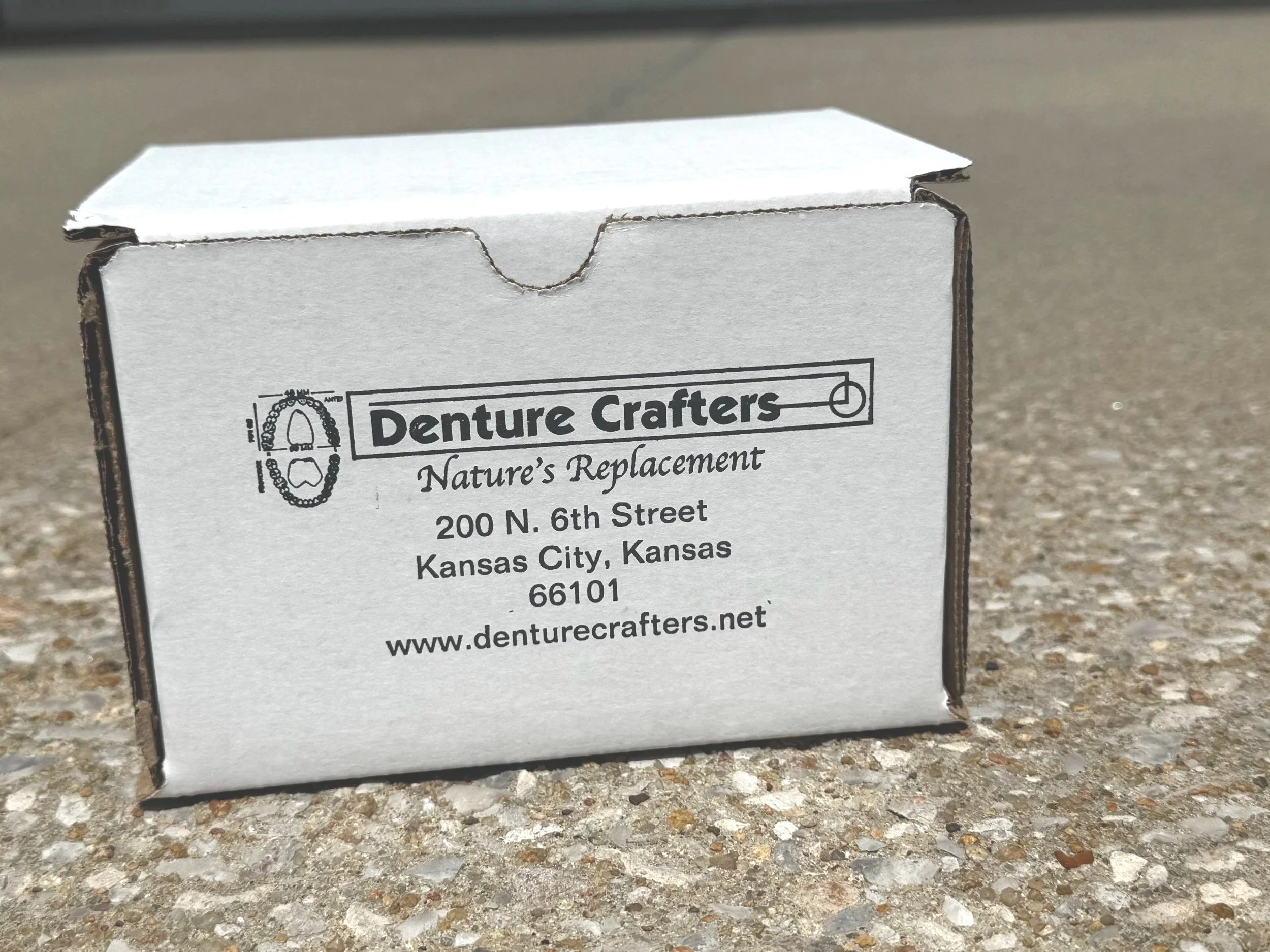 A cardboard box labeled for Denture Crafters, located in Blue Springs, Missouri. A top rated Dental Lab