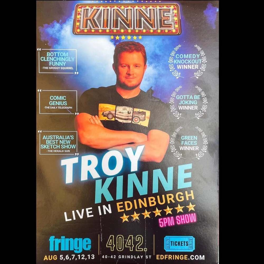 Poster promoting comedian Troy Kinne's live comedy show in Edinburgh, happening at 5 PM. Features a photo of Troy Kinne with his arms crossed, wearing a black t-shirt, against a backdrop of blue sky and clouds. The poster highlights various awards an