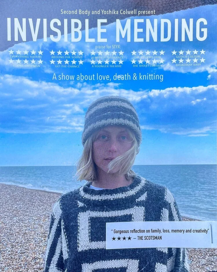 Poster for the play "Invisible Mending" featuring a woman with blonde hair, wearing a knit sweater and hat, standing on a pebble beach with the ocean and a partly cloudy blue sky in the background.