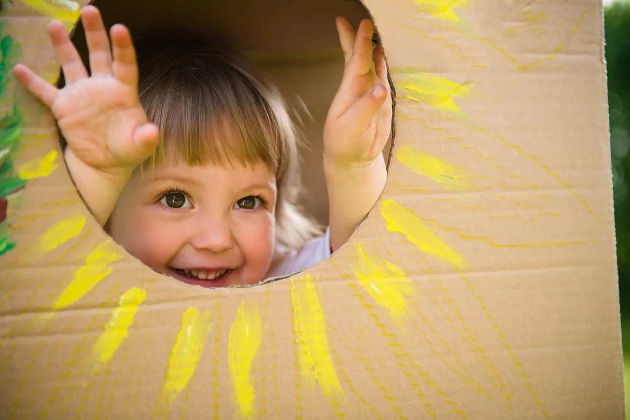little girl playing in a cardboard box with a painted sunflower during a speech therapy session