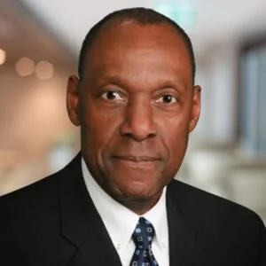 Headshot of a middle-aged African American man in formal attire, with a professional background.