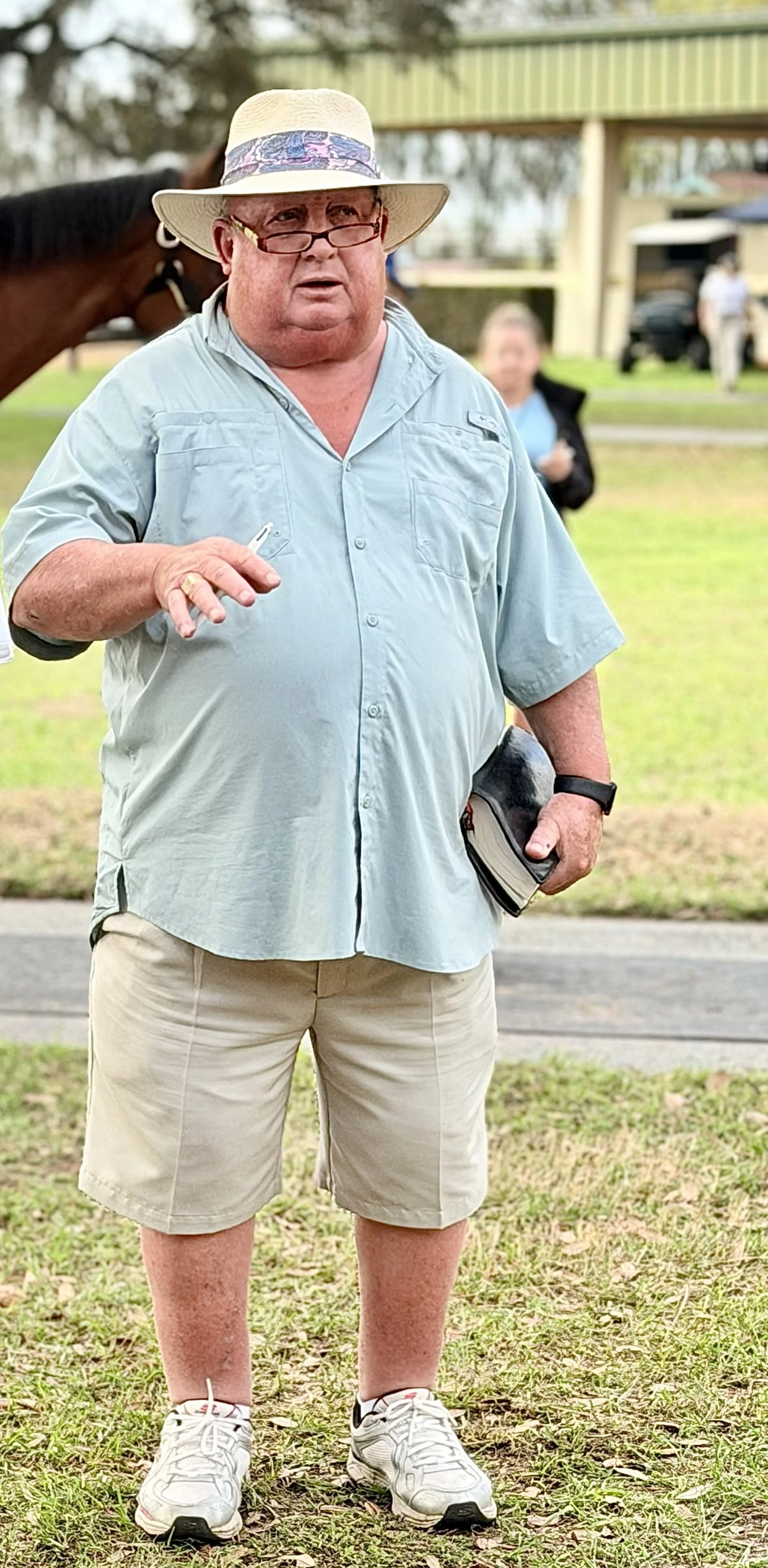 A racehorse and rider gallop on a dirt track at dawn with fog, trees, and a grassy area in the background, overlaid with the words 'New Castle Farm' in large, light blue, reflection-style text.