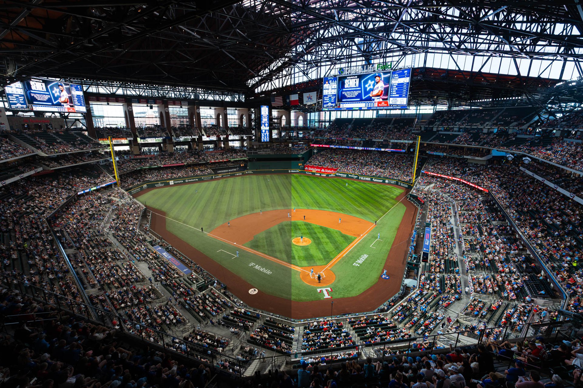 Inside a large baseball stadium crowded with spectators, green field with players, and large scoreboards above.