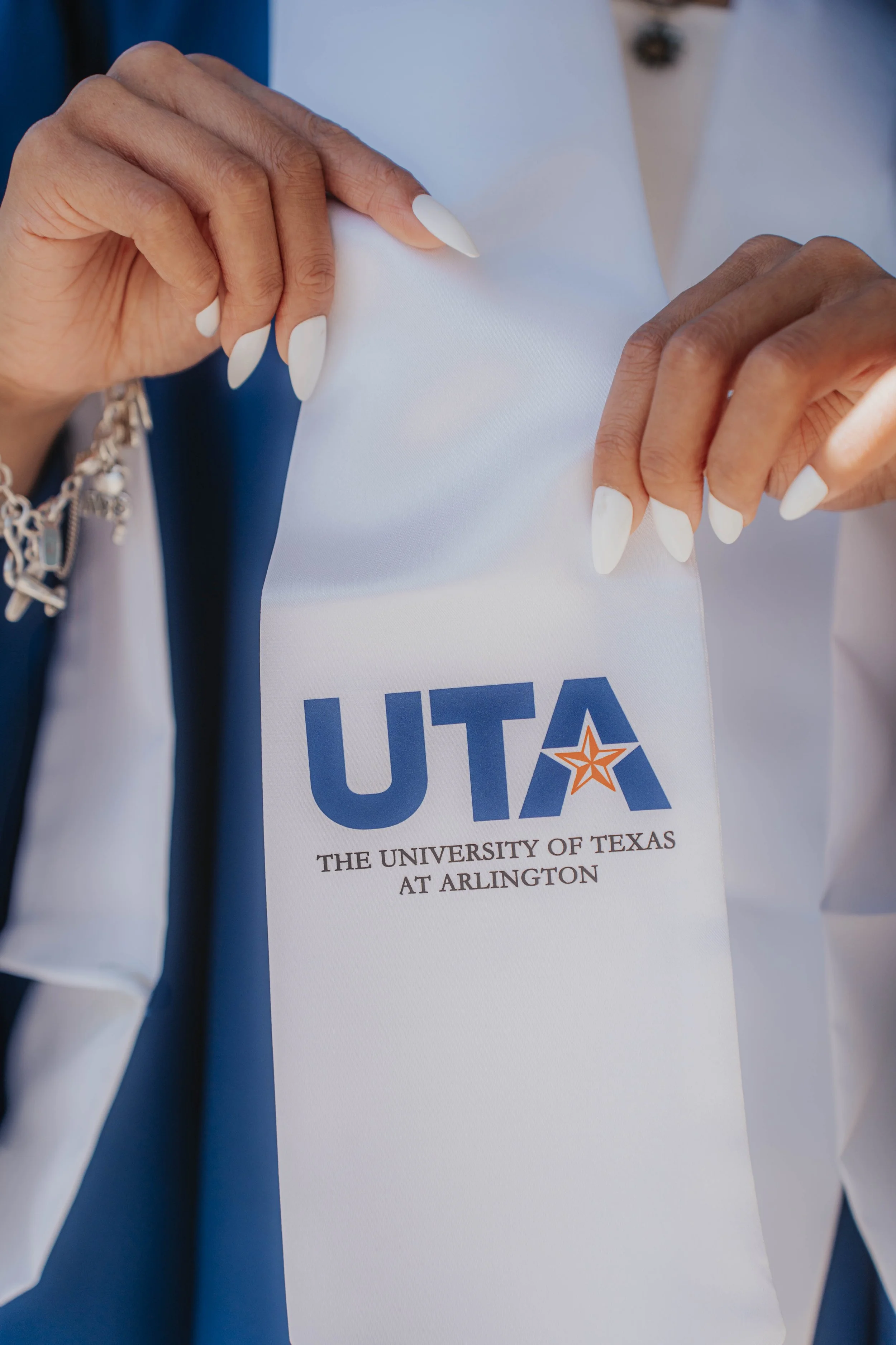 Close-up of hands holding a white sash with the Texas University at Arlington (UTA) logo and text.