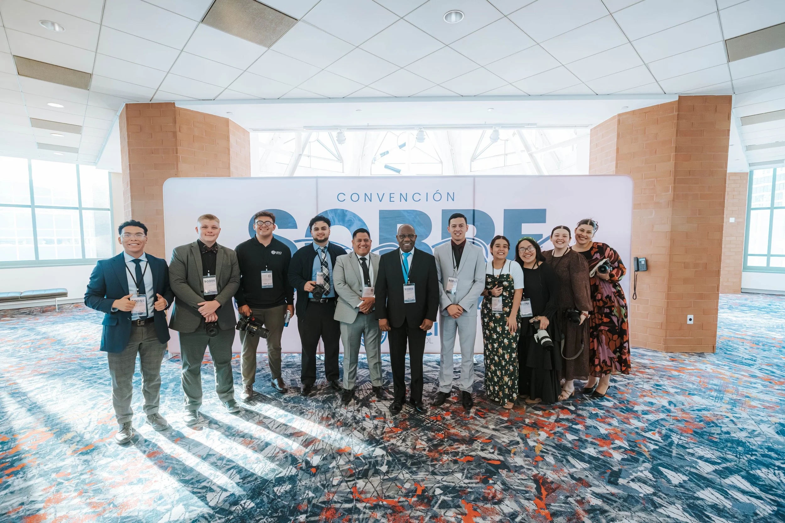 Group of diverse people attending a conference standing in front of a large sign that reads 'CONVENCIÓN SOBRE.'