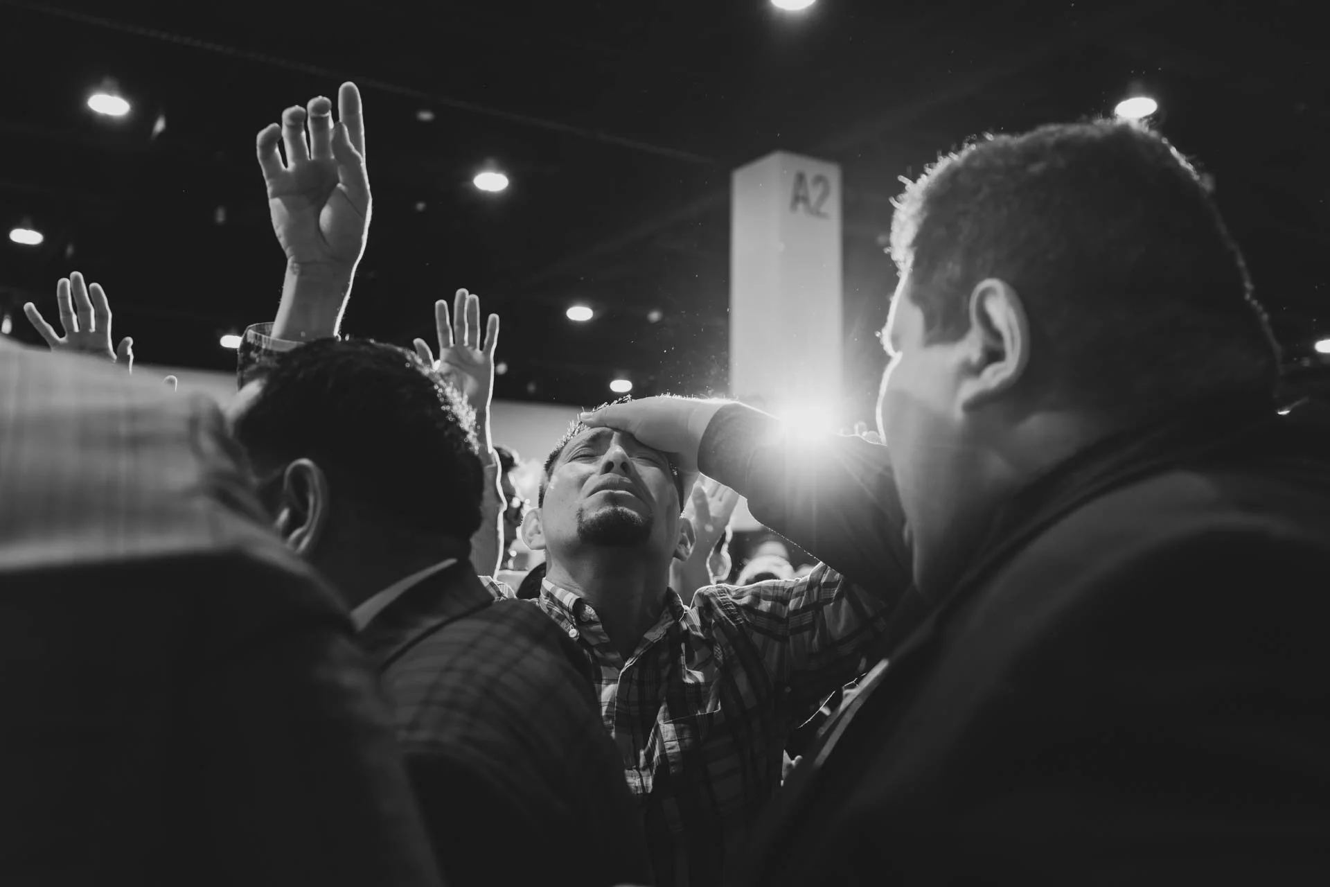 A black and white photo of several distressed individuals, with one person in the center with eyes closed and hand on forehead, others with hands raised, in what appears to be a crowded gathering or religious event.