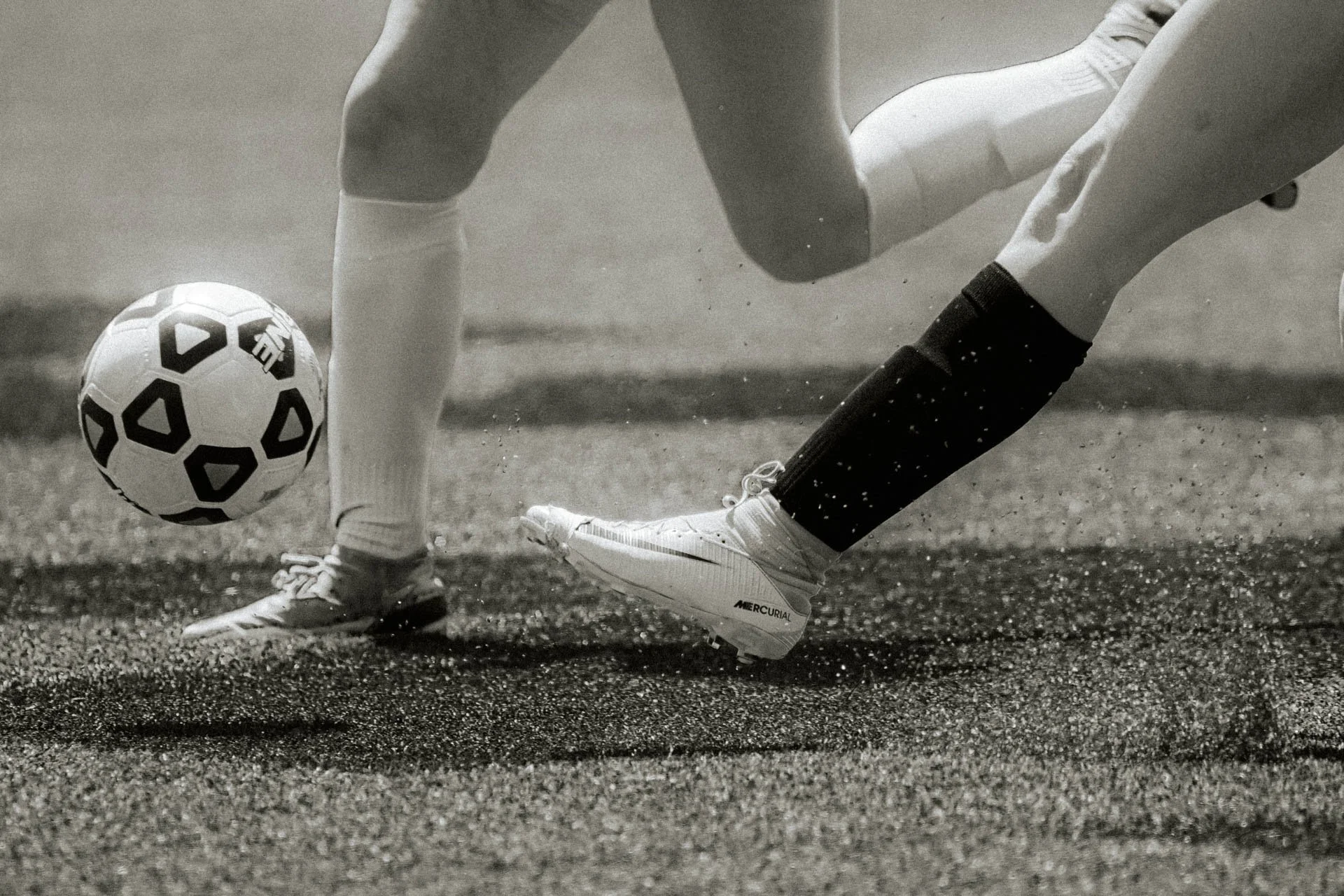 A soccer player in white cleats and black socks kicking a soccer ball on a textured surface.